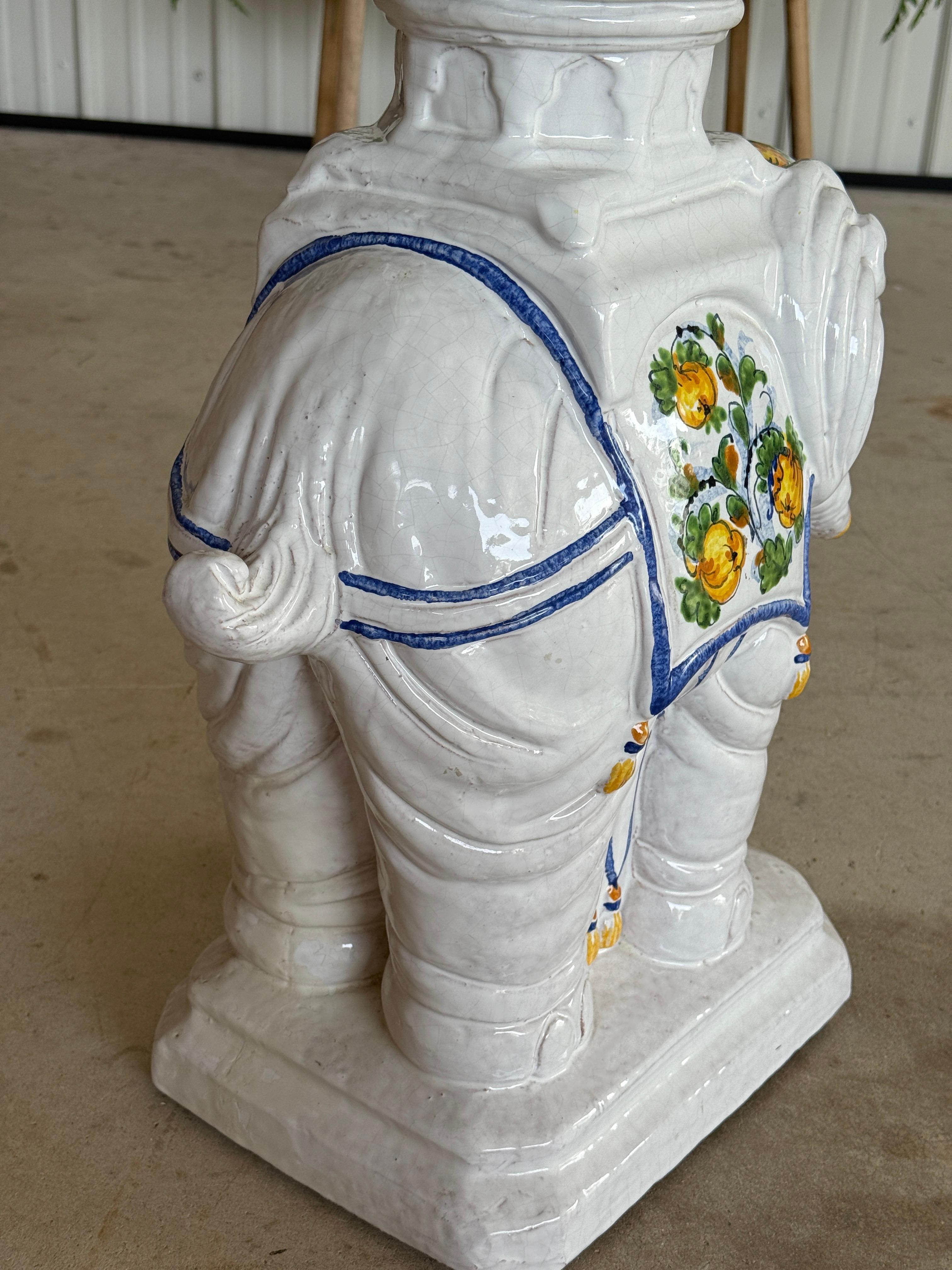 Caprichosa a la par que regia, esta mesa auxiliar elefante de terracota italiana vintage presenta una superficie ricamente esmaltada con vibrantes motivos florales y borlas pintados a mano en tonos amarillos, verdes y azules.
La escultural forma de
