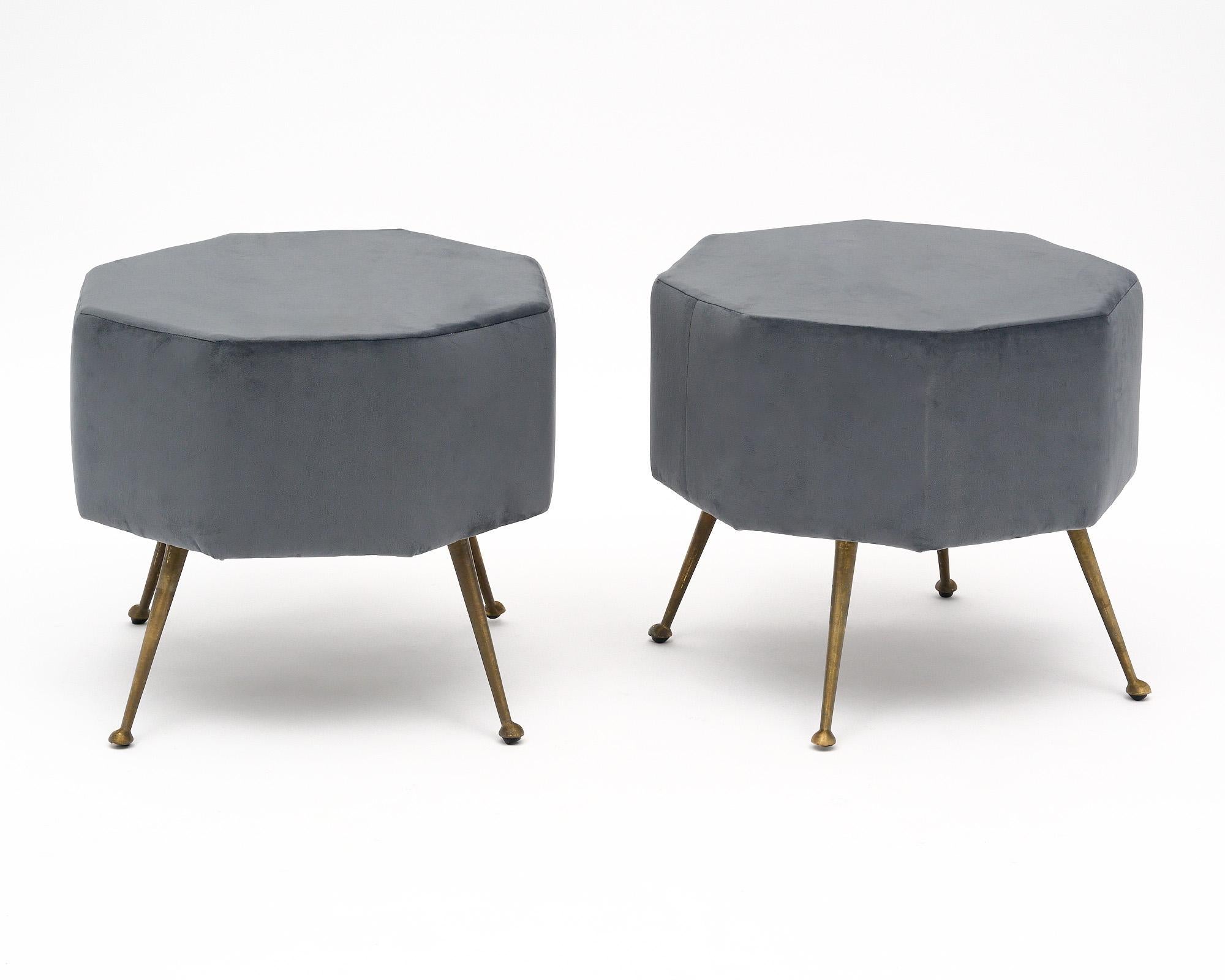Pair of Italian mid-century modern stools that have been newly upholstered in a gray colored micro fiber. Four original tapered, flared brass legs support the seat. The seat has an octagonal shape.

