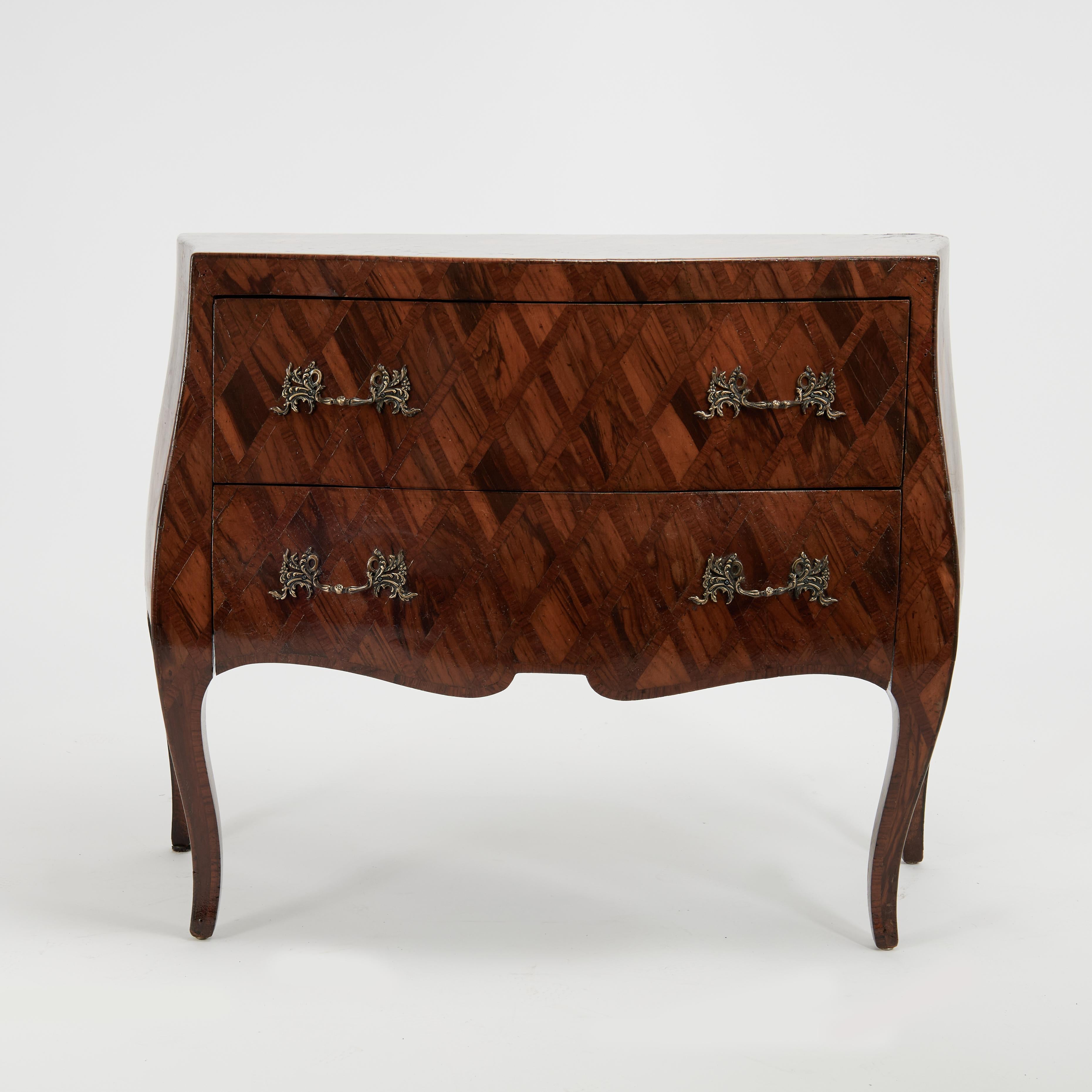 Elegante cassettiera italiana vintage a due cassetti realizzata in noce. In una scenografica forma bombay con ferramenta in ottone e gambe a cabriola, presenta un esclusivo motivo a intarsio in stile arlecchino.