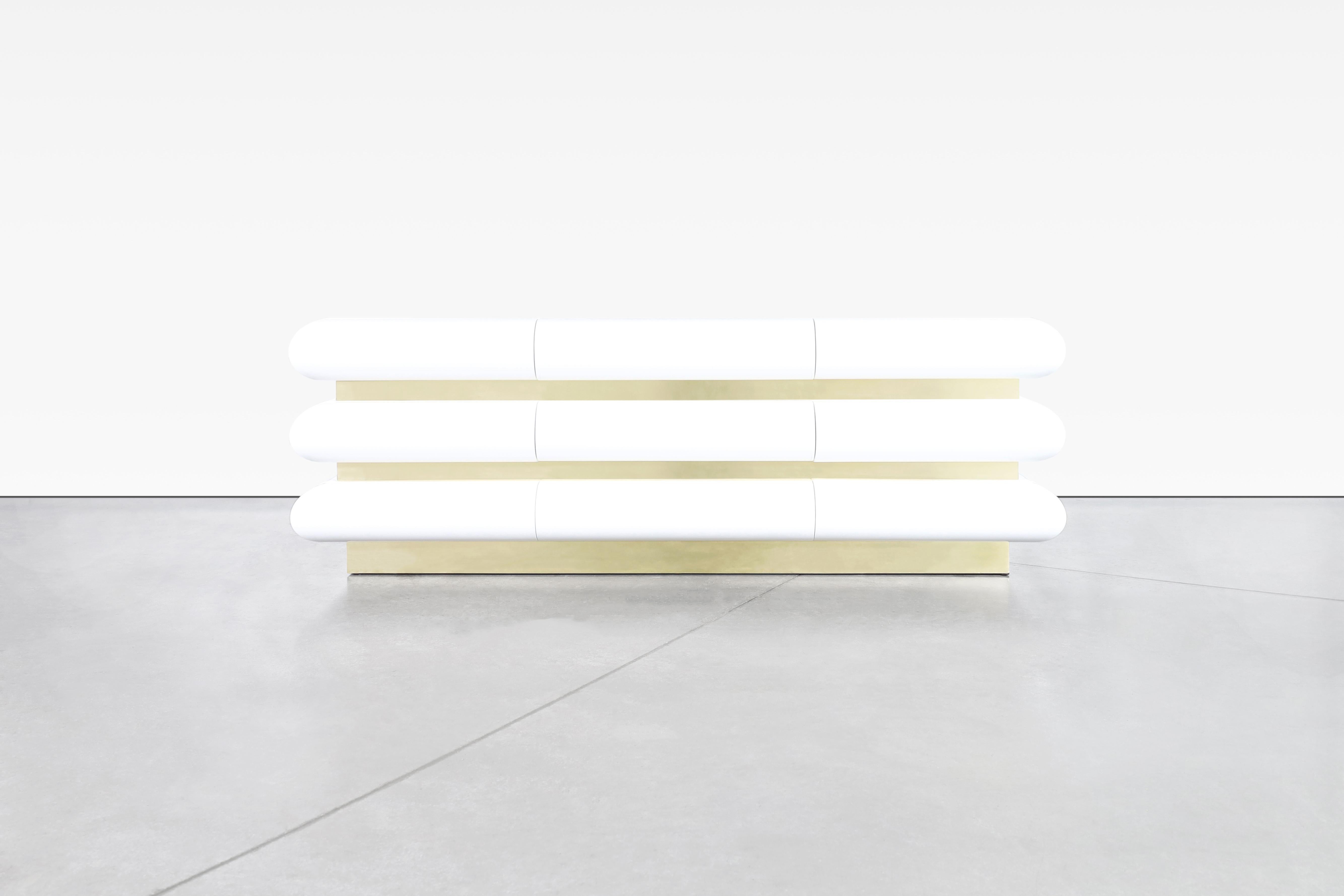 Questo bellissimo comò è uno splendido esempio di design italiano degli anni Ottanta. È stato restaurato professionalmente con una finitura laccata bianca lucida che gli conferisce un aspetto moderno e sofisticato. La base è rivestita in ottone e le