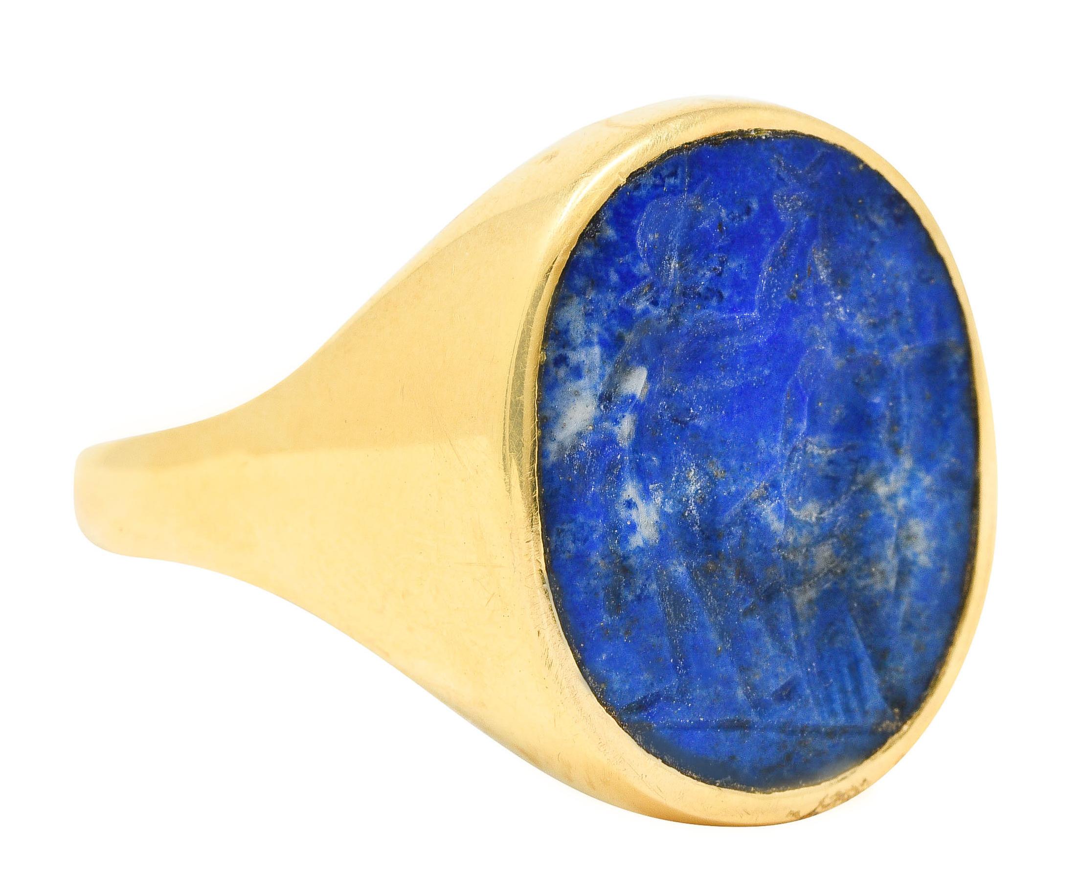 Signet ring centers a bezel set oval shaped lapis lazuli slab with an intaglio carving of two figures

Opaque ultramarine blue with white mottling and subtle pyrite flecking - measuring 17.0 x 13.0 mm

Figures are depicted in draped clothing with
