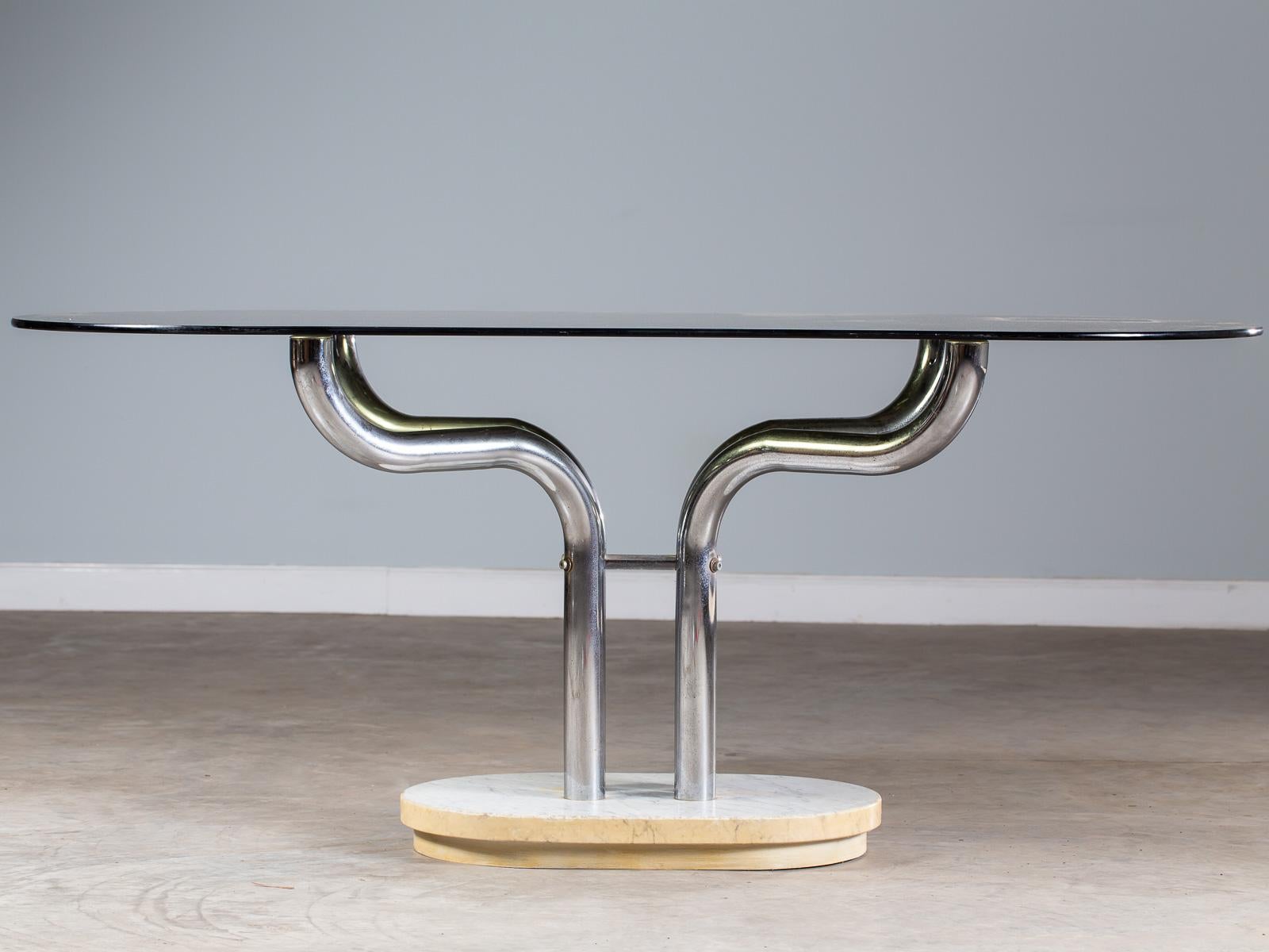 A fabulous period Italian vintage dining writing table circa 1970 having an oval marble base and four curved chrome metal legs supporting the original smoked glass racetrack shaped oval top. The sensuous curves of this Italian table are superb from