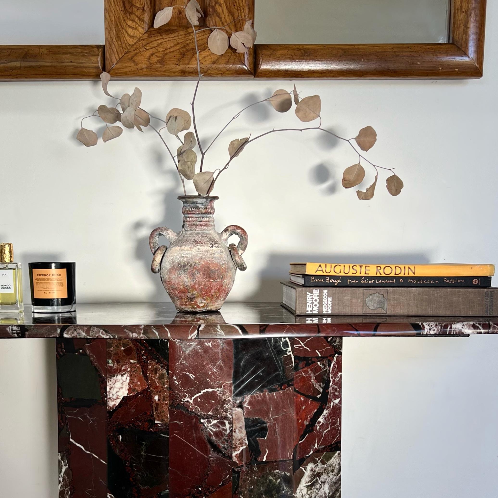 A vintage Italian marble console, circa late 1970s. Tones of oxblood, graphite, and bone in composite flagstone motif. The top widens in the center and is more narrow at the edges, and the base is also a bit wider at the center. Signs of age include