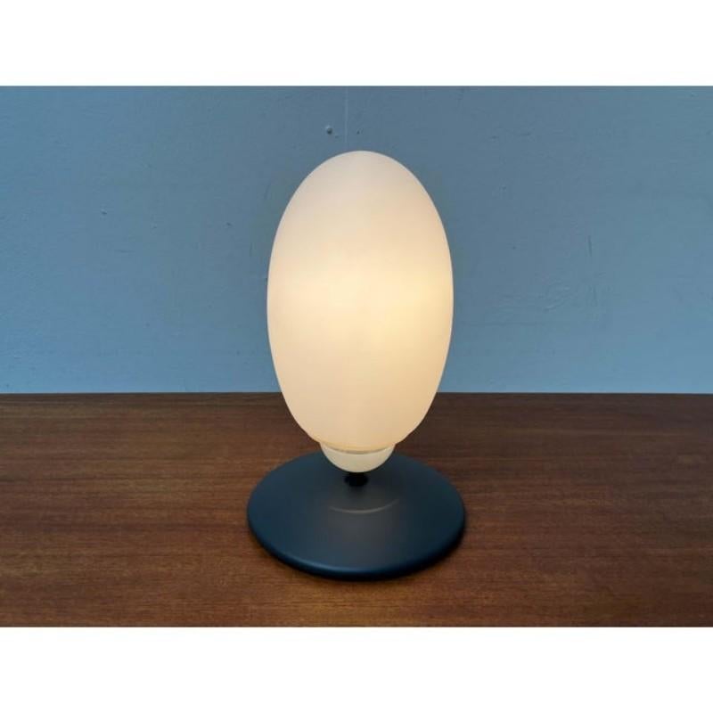 The table lamp version from the Brera series by Flos, designed by Achille Castiglioni.

A very simple and elegant table lamp. The egg-shaped opal glass lamp body sits on a short, slender metal shaft. At the lower end, the shaft transitions into a