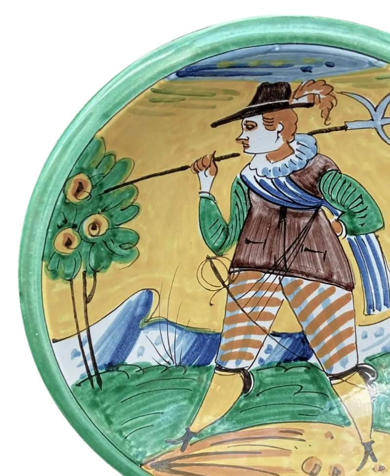 This beautiful maiolica pottery charger is from Montelupo, Italy and is boldly decorated with a soldier walking, carrying a tool of the day. Vividly painted in yellow, green, and blue. Condition is excellent, no chips or scratches.