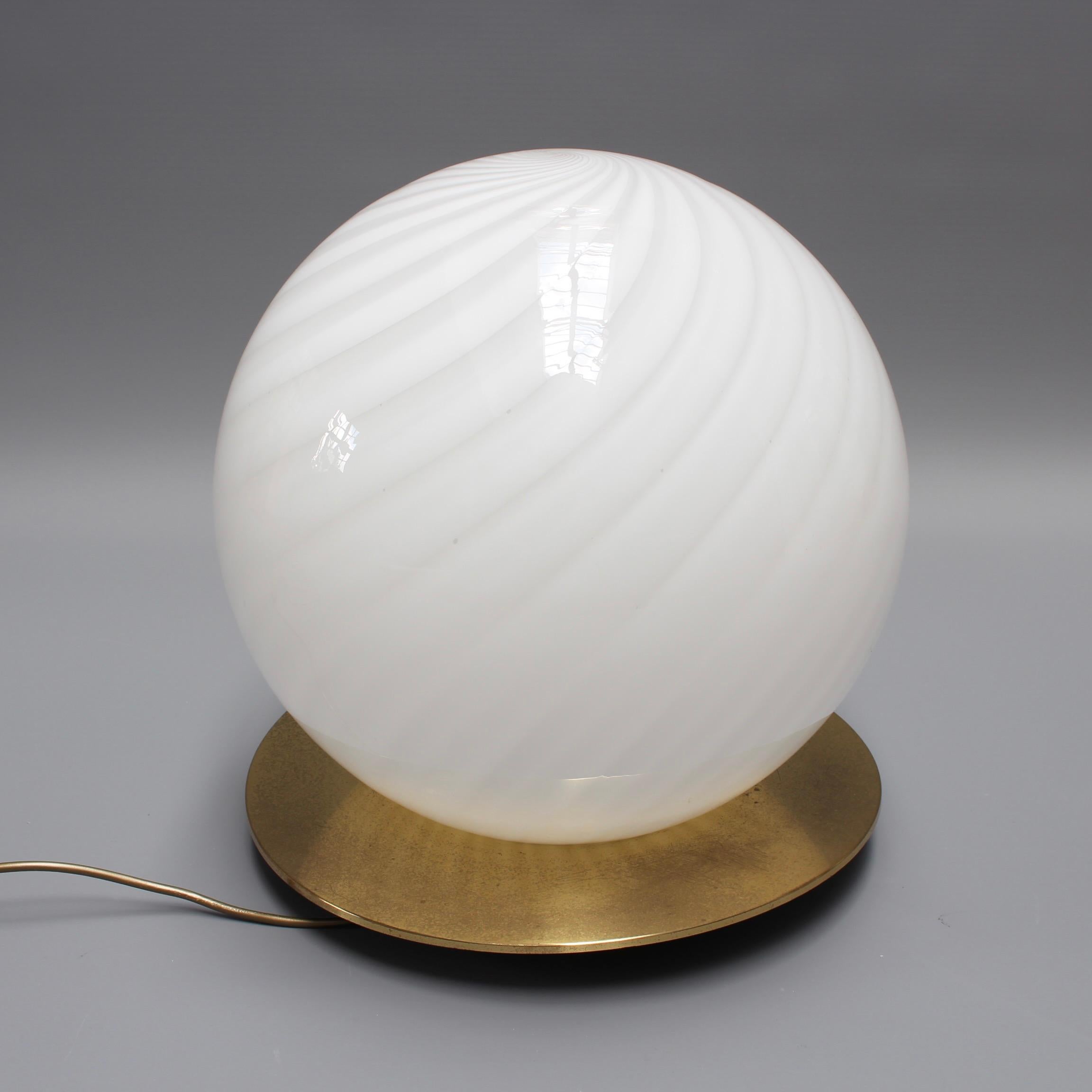 A large 1970s Italian Murano glass globe table lamp. Modernist and elegant, this blown Murano table lamp provides a source of lighting which is both utilitarian and decorative. The swirling longitudinal lines both capture and amplify the light's