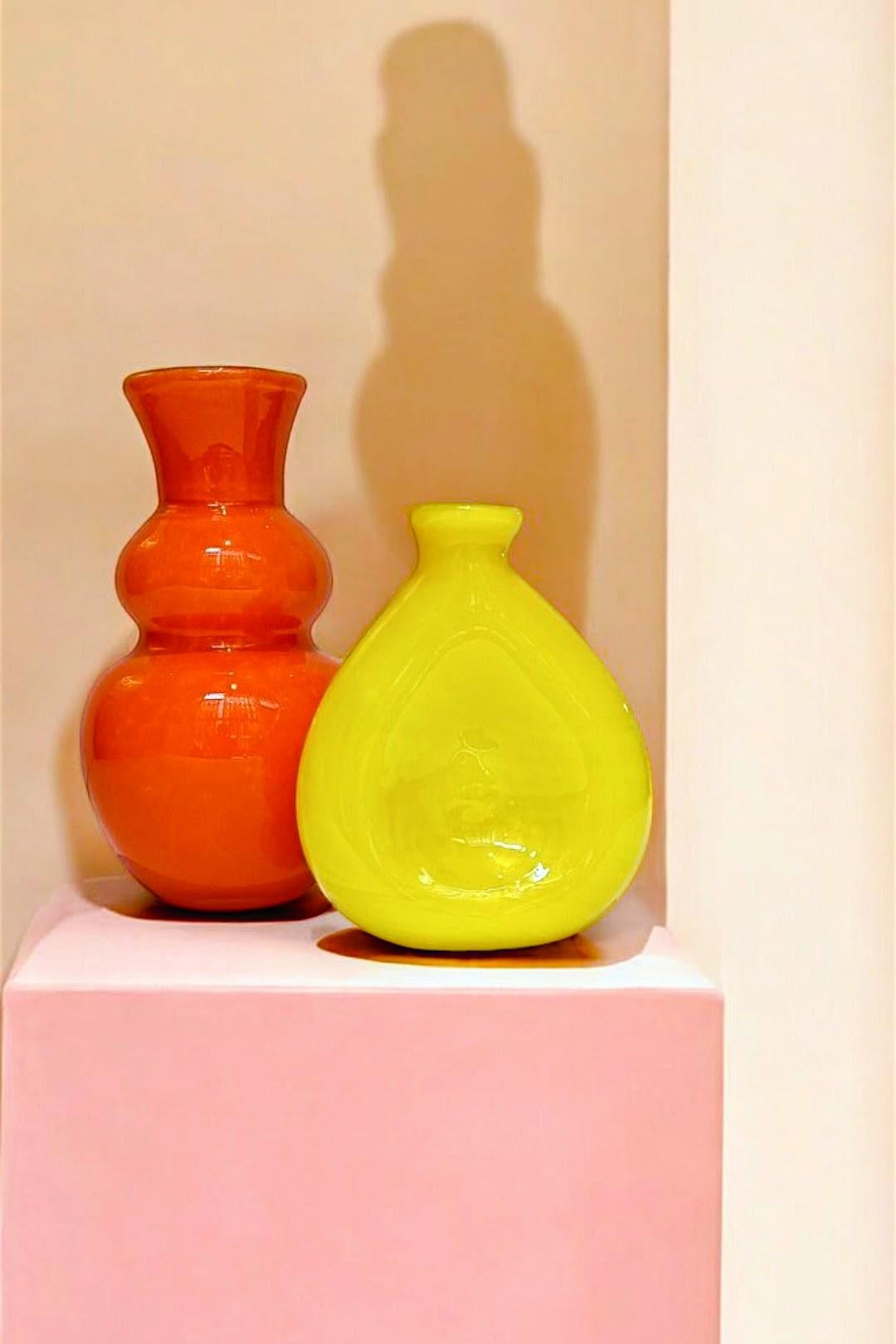 Pair of vintage Pop Art style Mid-Century Modern Murano glass vases. Their thick exterior layers in vibrant orange and yellow hues, along with the distinctive white casing on the orange vase, add a striking visual appeal. They were handcrafted in