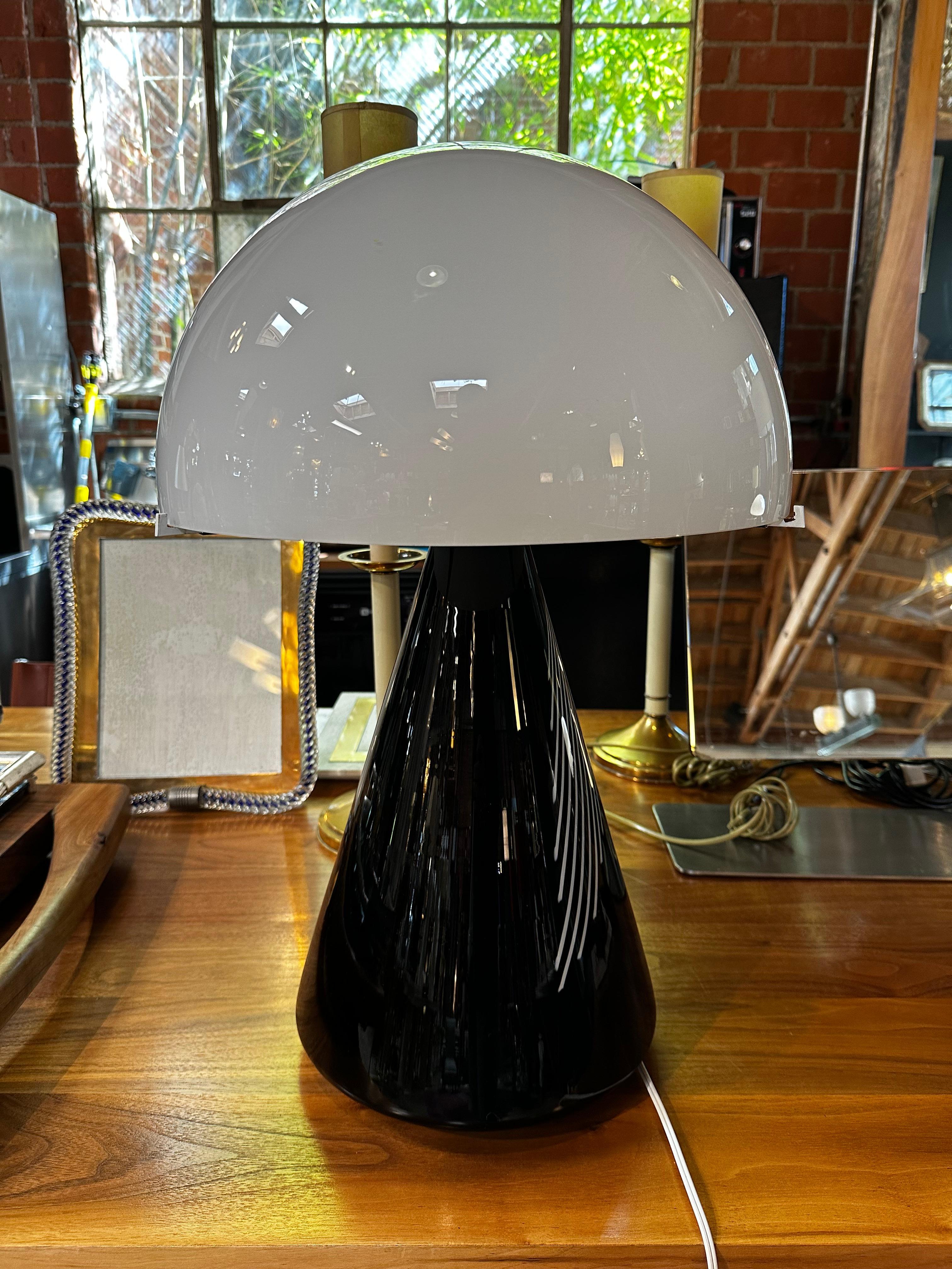 The Mushroom full blass table lamp made by Leucos in the 1980s features a stylish black glass base and a white glass shade. The overall design of the lamp resembles a mushroom, with the shade curving outward like a cap. The glass construction allows