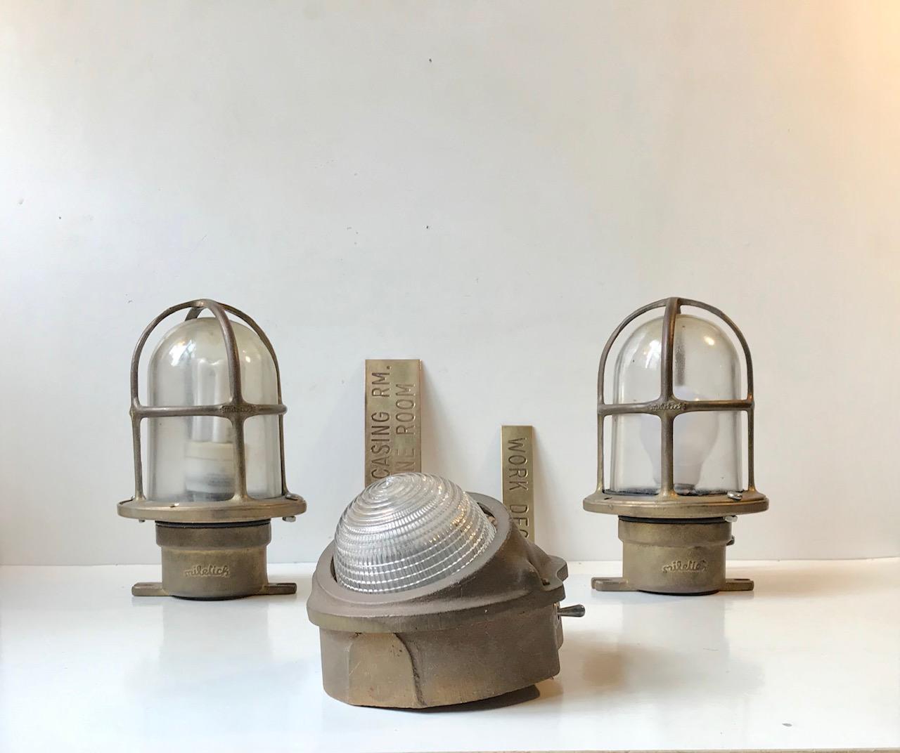 A trio of Italian Maritime bronze sconces with caged glass. They have been mounted on a Norwegian Naval ship. Two of them came from the engine room and the last one hang over the door to the work deck. The two brass signs are included in this lot.