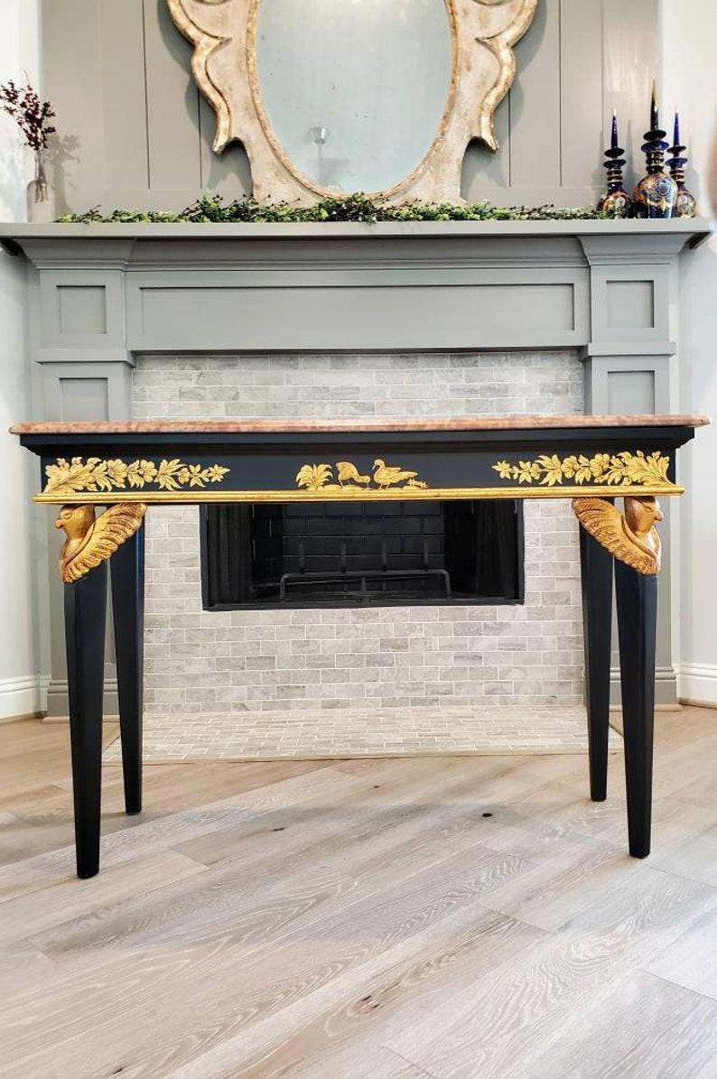 An Italian Rococo Neoclassical console table, dating to the mid-20th century, having a black lacquered rectangular shaped base prominently featuring fantastical avian giltwood carvings on the front legs, an apron embellished with painted gilt gold