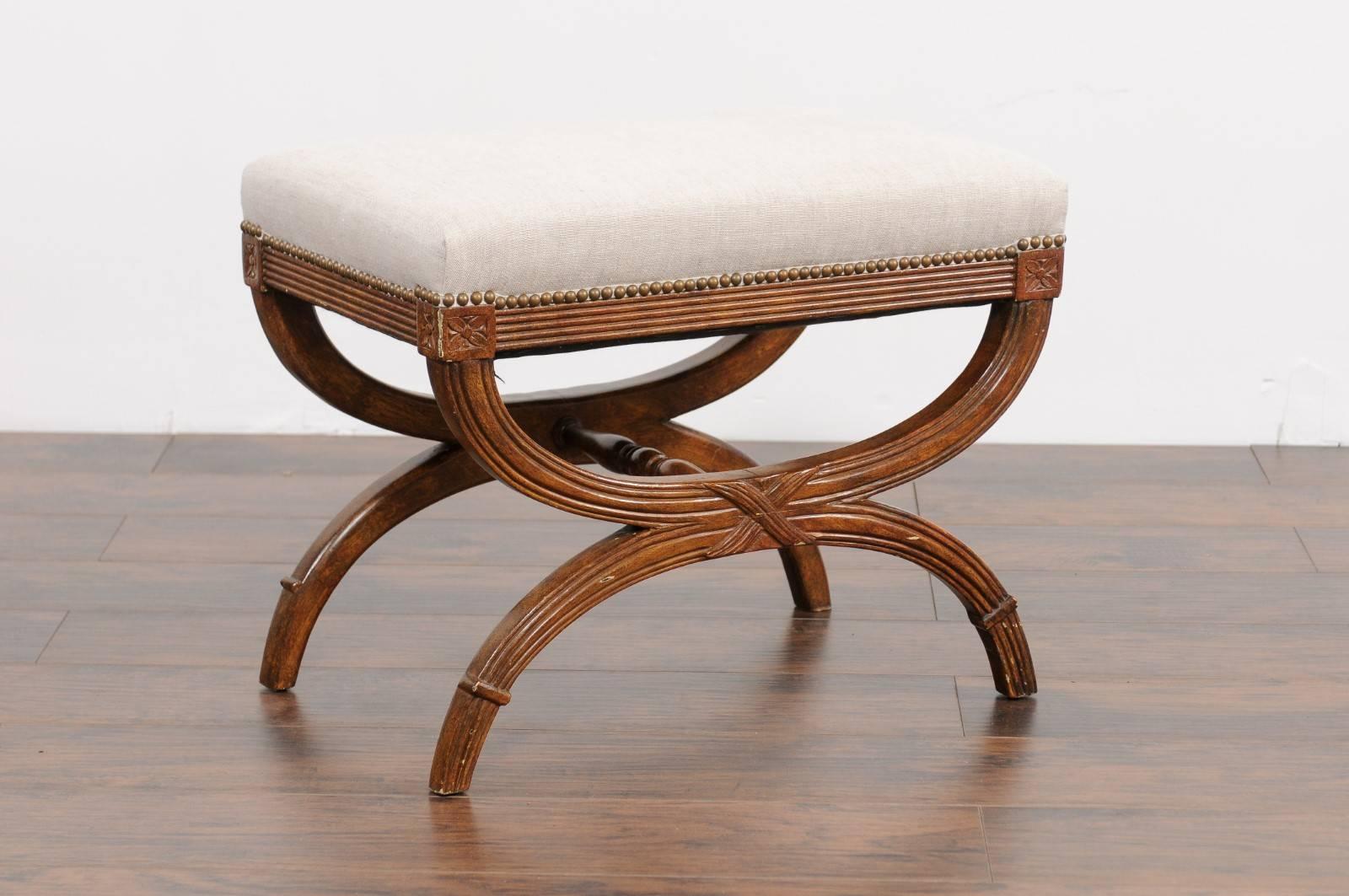 An Italian vintage neoclassical style carved and grain painted X-form stool from the mid-20th century with new upholstered seat. This Italian stool features a rectangular seat, upholstered in a simple linen fabric, accented with a brass nailhead