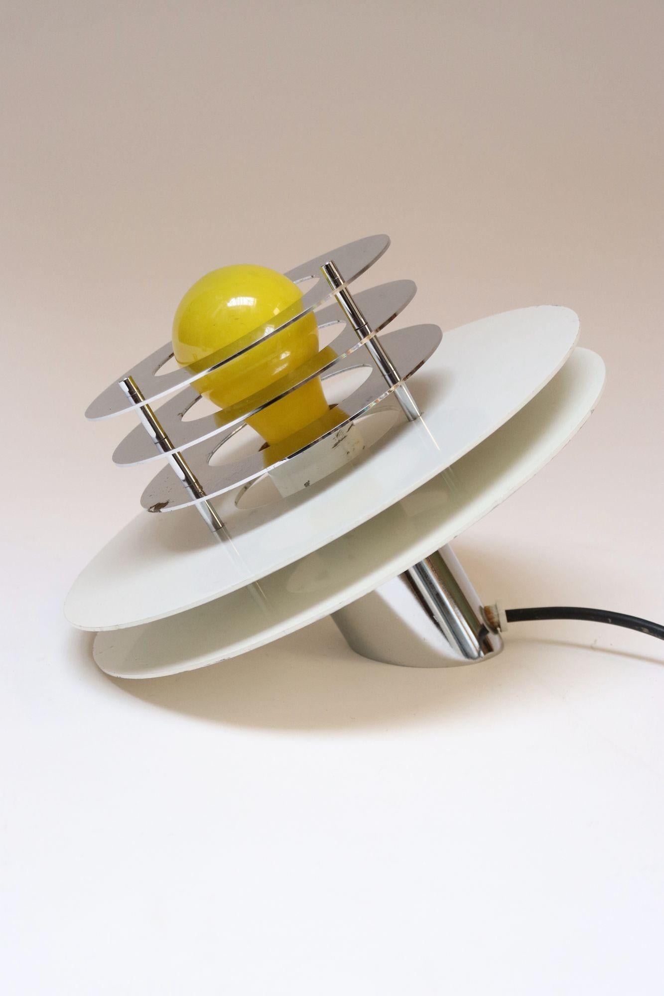 Italian Modernist table lamp, ca. 1960s, composed of a chromed-metal oblique cylindrical base supporting two white lacquered metal discs bracketed to three smaller chrome disks.
Unique, asymmetrical form resembling a tilted/angled flying