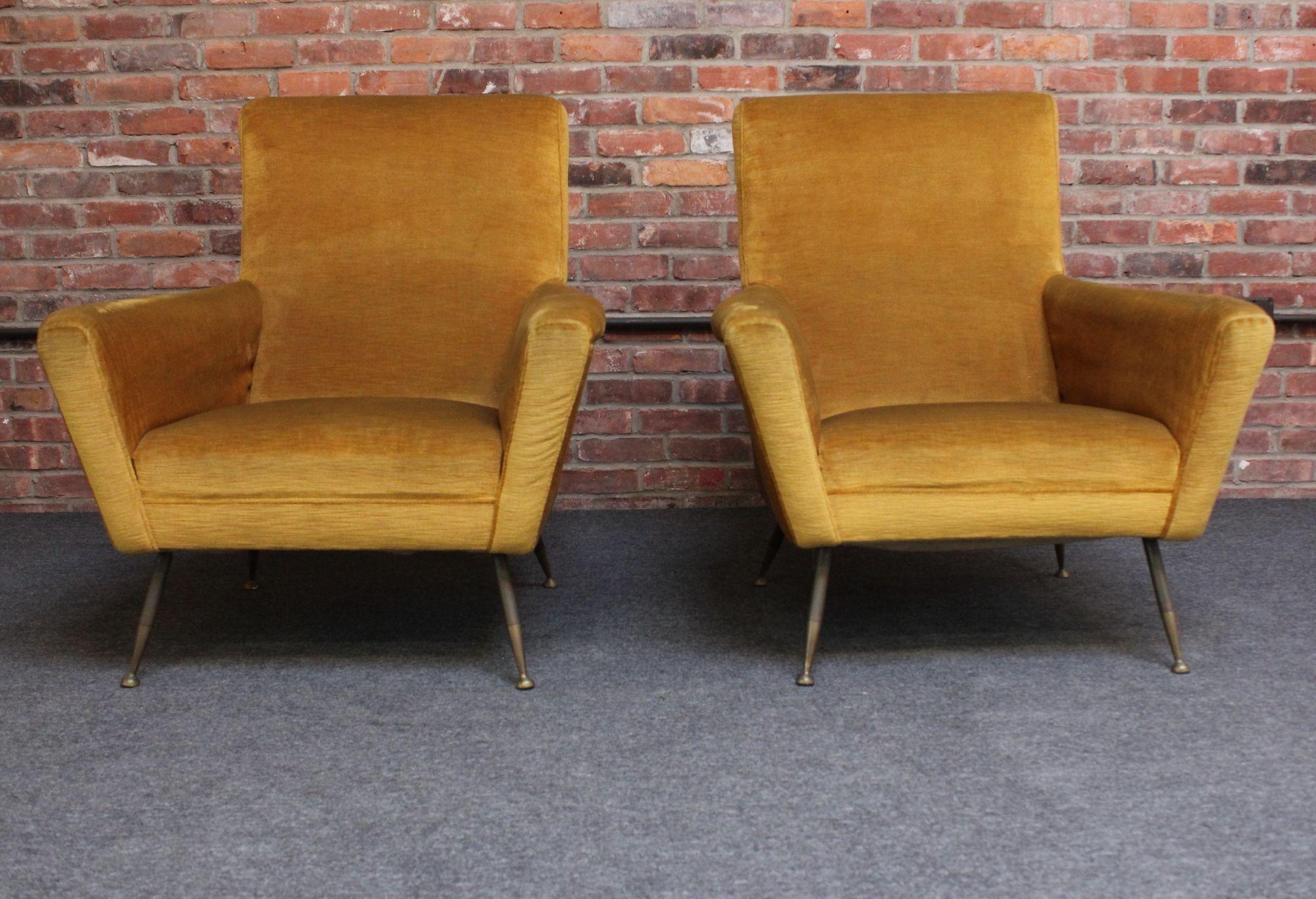Mid-20th Century Italian Modernist lounge/arm chairs in original ochre cotton velvet upholstery (ca. 1960s, Italy).
Low slung form with wide, sculptural arms, all supported by four splayed, two-tone brass legs.
Original upholstery shows wear