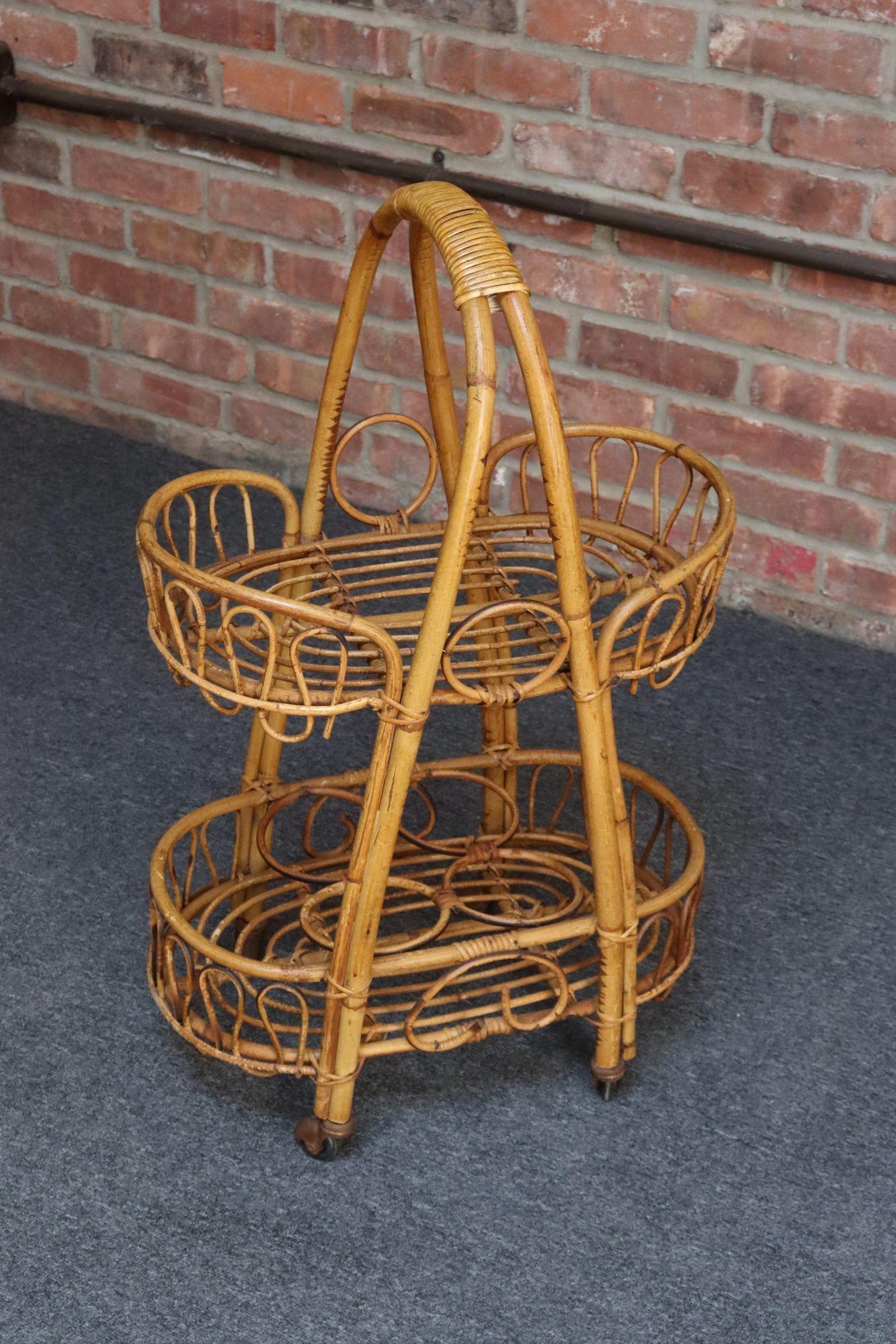 Chariot de bar / trolley / serveur roulant en bambou tressé, osier et rotin (vers les années 1960, Italie).
Deux niveaux ovales (l'un ouvert, l'autre équipé de supports pour quatre bouteilles) avec des surfaces en osier courbé en forme de spirale et