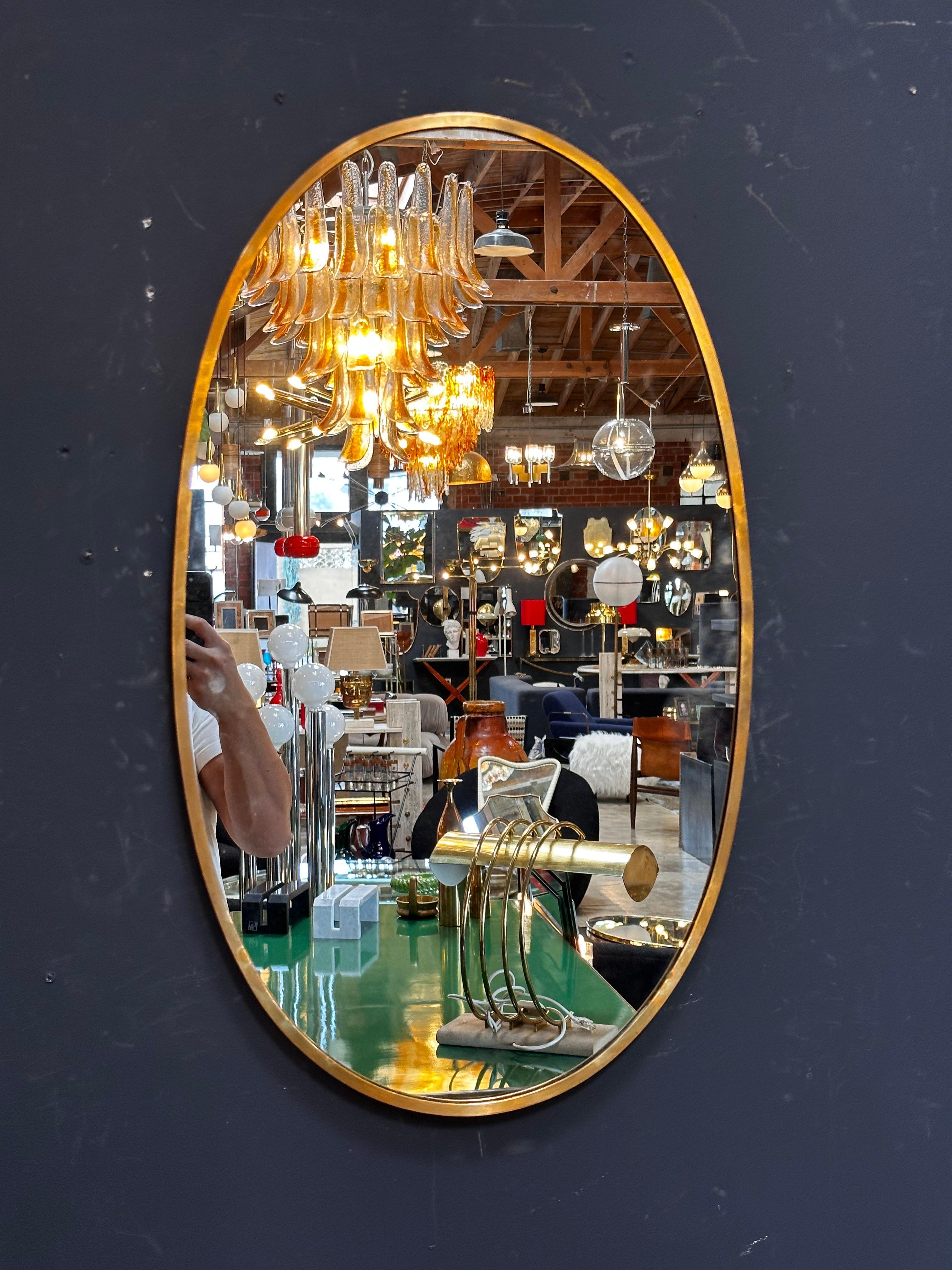The Vintage Italian 1980s Oval Brass Wall Mirror exudes elegance with its timeless oval shape and exquisite brass frame.

