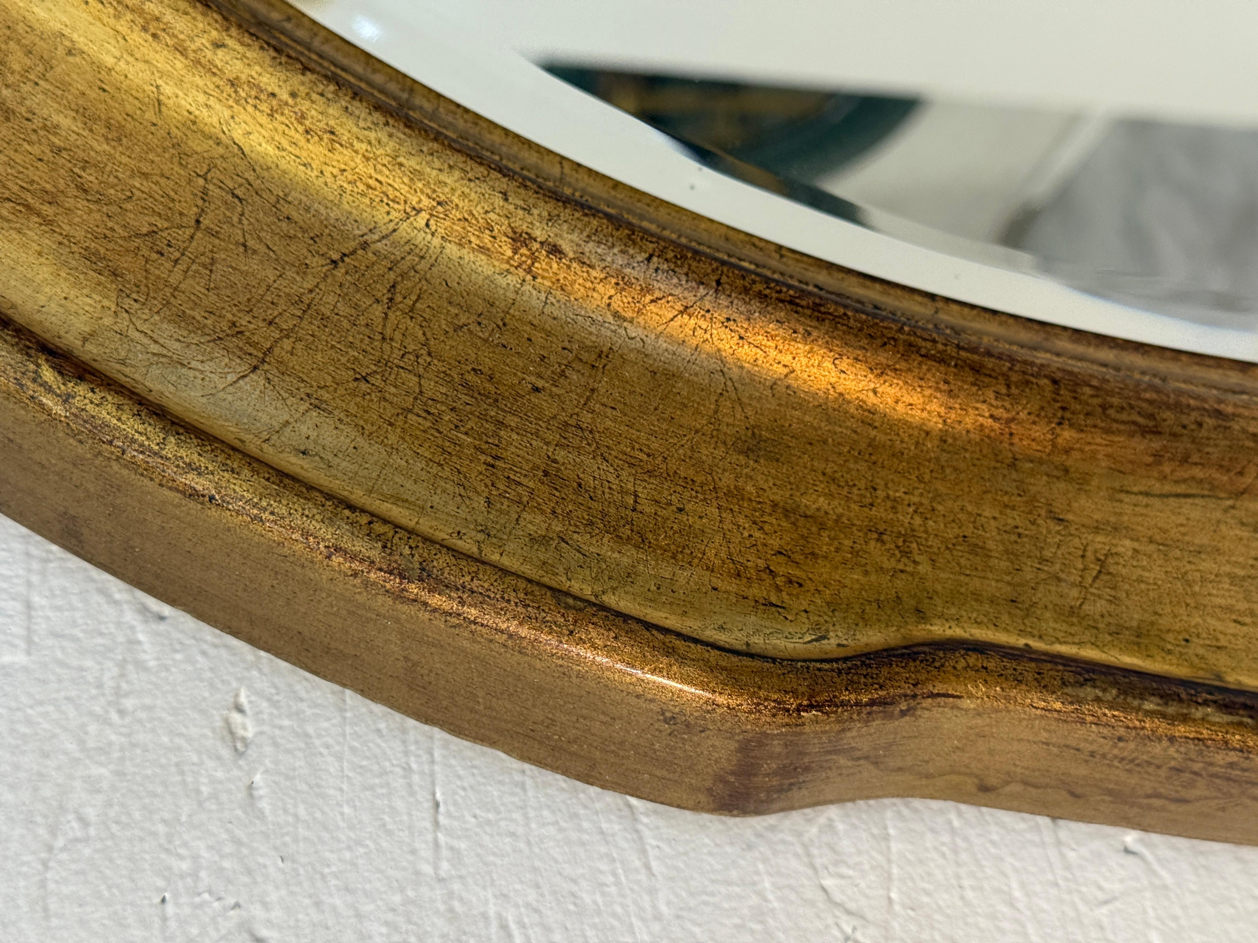 Charmanter ovaler italienischer Wandspiegel im Vintage-Stil mit handvergoldetem Holzrahmen und dezentem Wellenschliff. Das warme Goldfinish zeigt eine schöne gealterte Patina, die dem Stück Tiefe und Charakter verleiht. Das abgeschrägte Glas