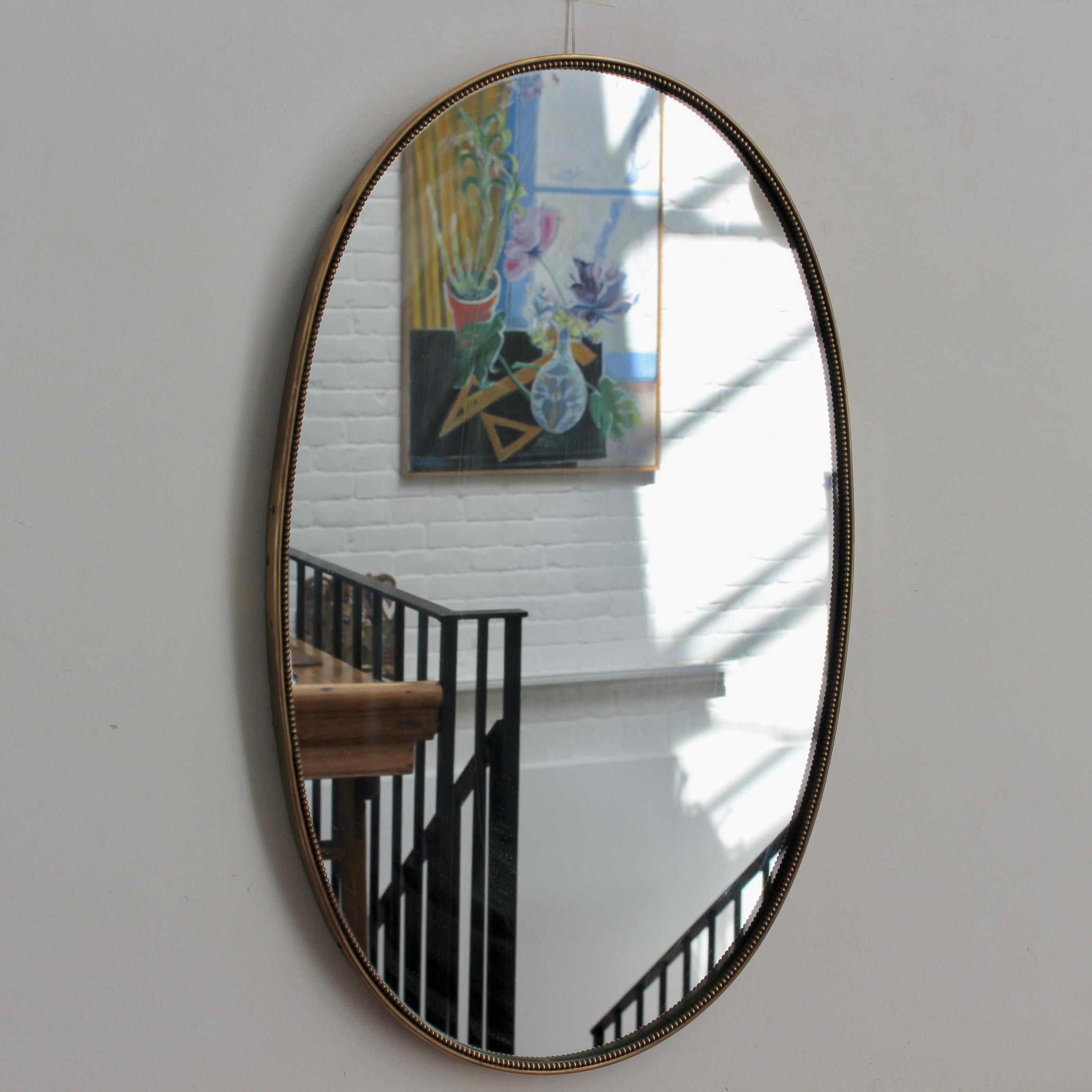 Mid-century Italian wall mirror with brass frame (circa 1950s). The mirror is oval in shape, very smart with irresistible durability. The visual impression is elegant and very unique in a modern Gio Ponti style. A distinctive beading outlines the