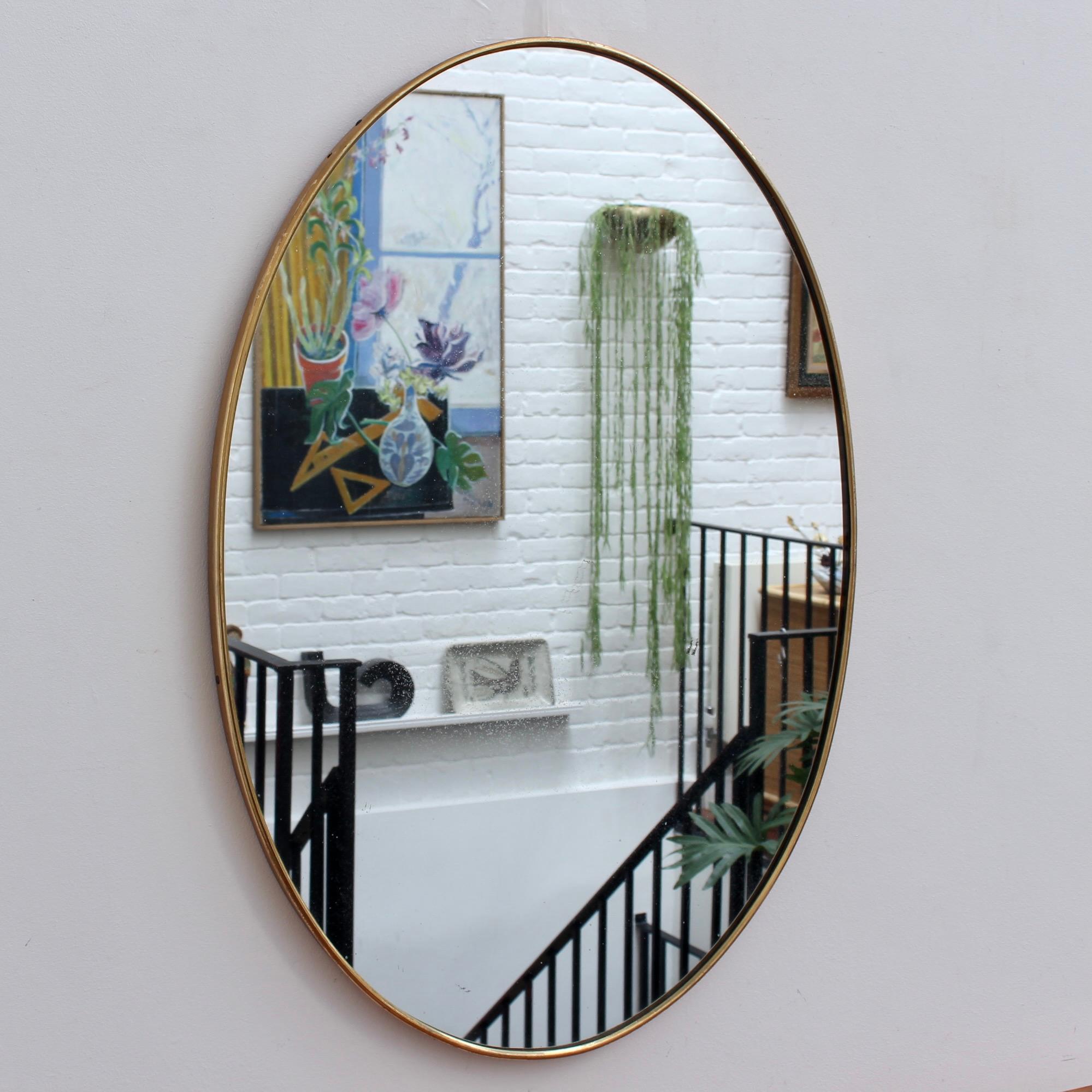 Mid-century Italian wall mirror with brass frame (circa 1950s). The mirror is oval in shape and very smart with rugged durability. The visual impression is elegant and very distinctive in a modern Gio Ponti style. In overall good condition with