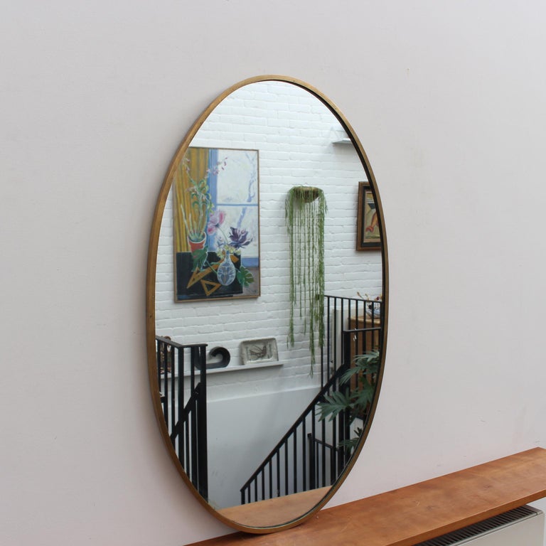 Mid-century Italian wall mirror with brass frame (circa 1950s). The mirror is oval in shape and very smart with rugged durability. The visual impression is elegant and very distinctive in a modern Gio Ponti style. The mirror is in good overall