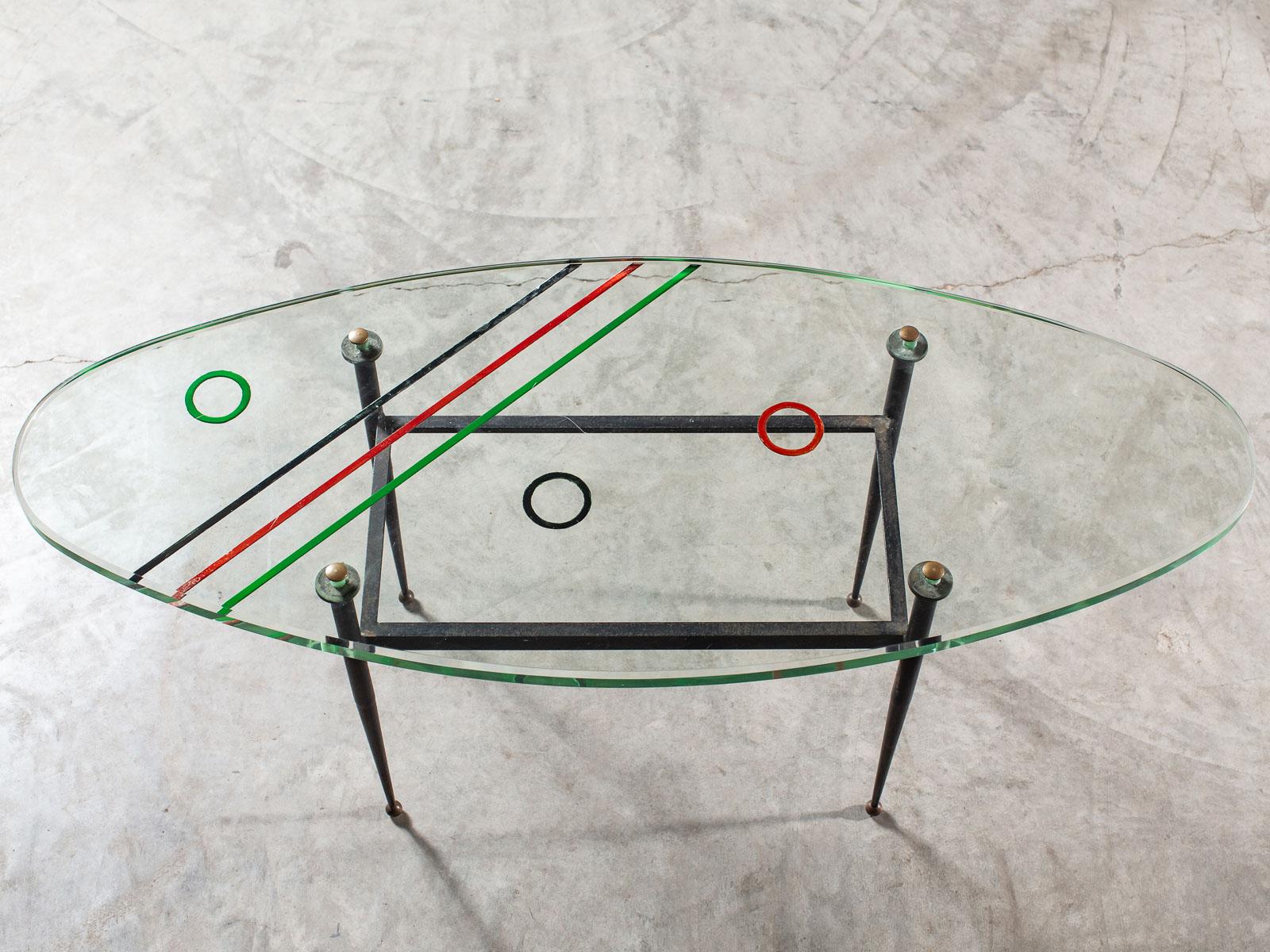 This vintage oval Italian coffee table circa 1960 has an intriguing design. The thick oval glass top has been deeply etched on the underside with a pattern of stripes and circles and then painted in red, green and black. So while it looks as if the
