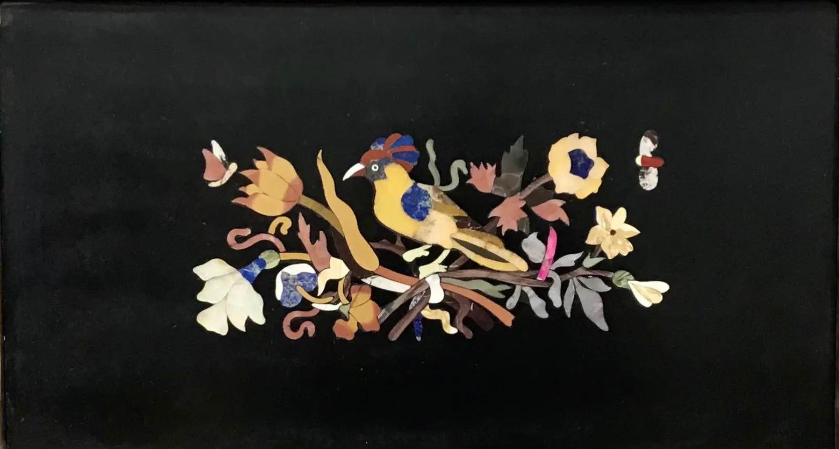 Italian Pietra Dura Bird Plaque. Depicts colorful bird made of precious stone inlaid on black marble, standing on a branch having flowers and leaves, also precious stone. Above are butterfly in flight. The silver gilded frame is original to the