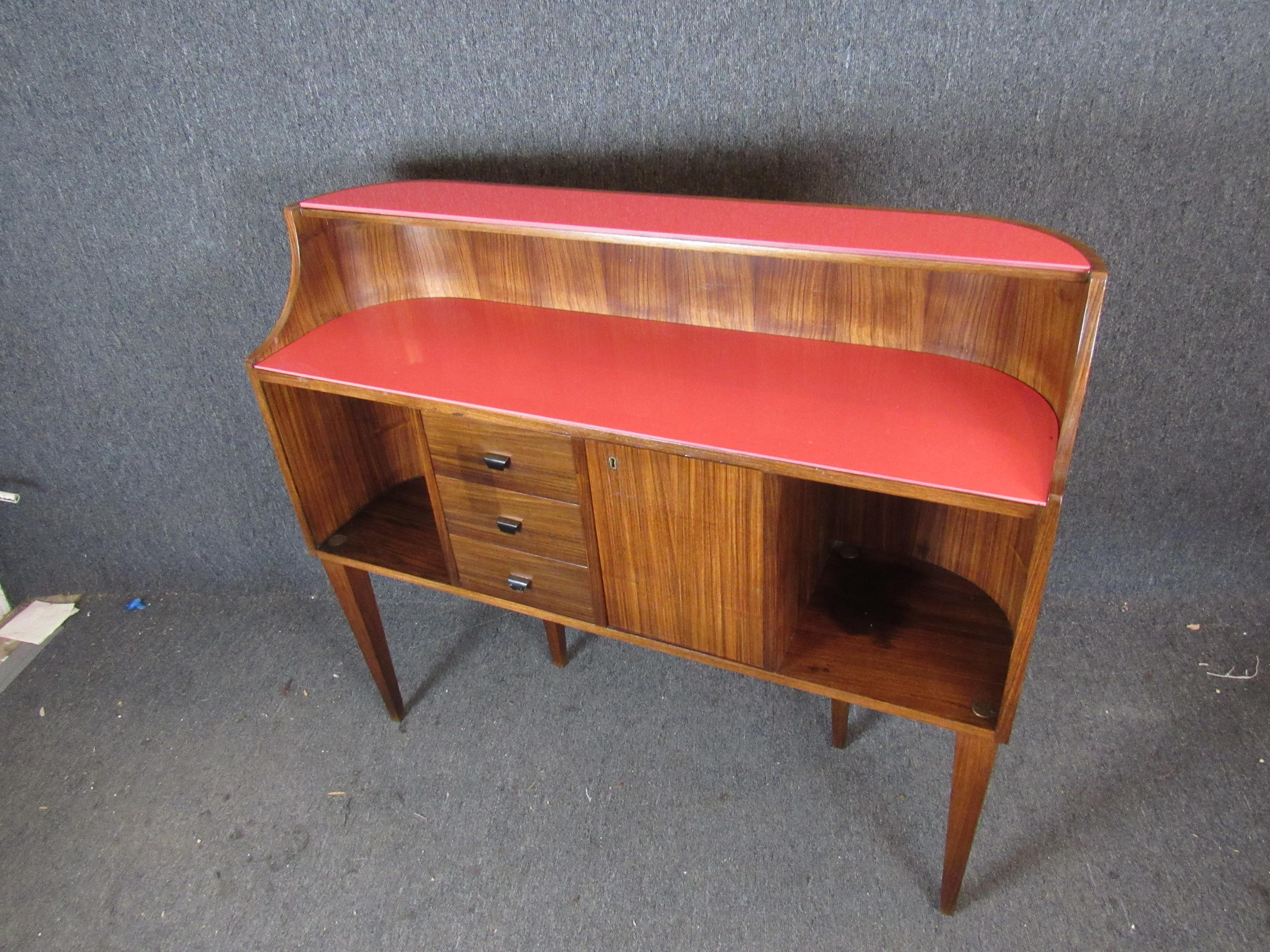 This stunning midcentury vintage Italian console bar shows off a gorgeous walnut wood grain and brings an extra pop of color with funky coral pink glass tops. Two curved open cabinets and three pull-out drawers offer plenty of storage an
