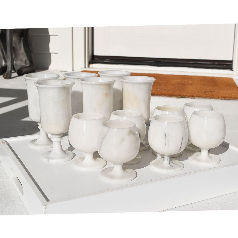 A lovely set of 13 hand-carved footed wine glasses or goblets. This set of drinking glasses are hand-carved and created from Carrara marble. Each cup is carved in one solid piece of stone with a round hand-turned base. The veining on each piece