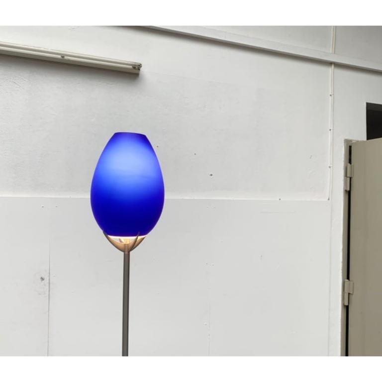 Elegante lámpara de pie de cristal del fabricante italiano Lucente.

El llamativo difusor de cristal está revestido de azul mate y se asienta en el extremo de un esbelto eje. La parte superior del eje es de color plata mate y la inferior gris