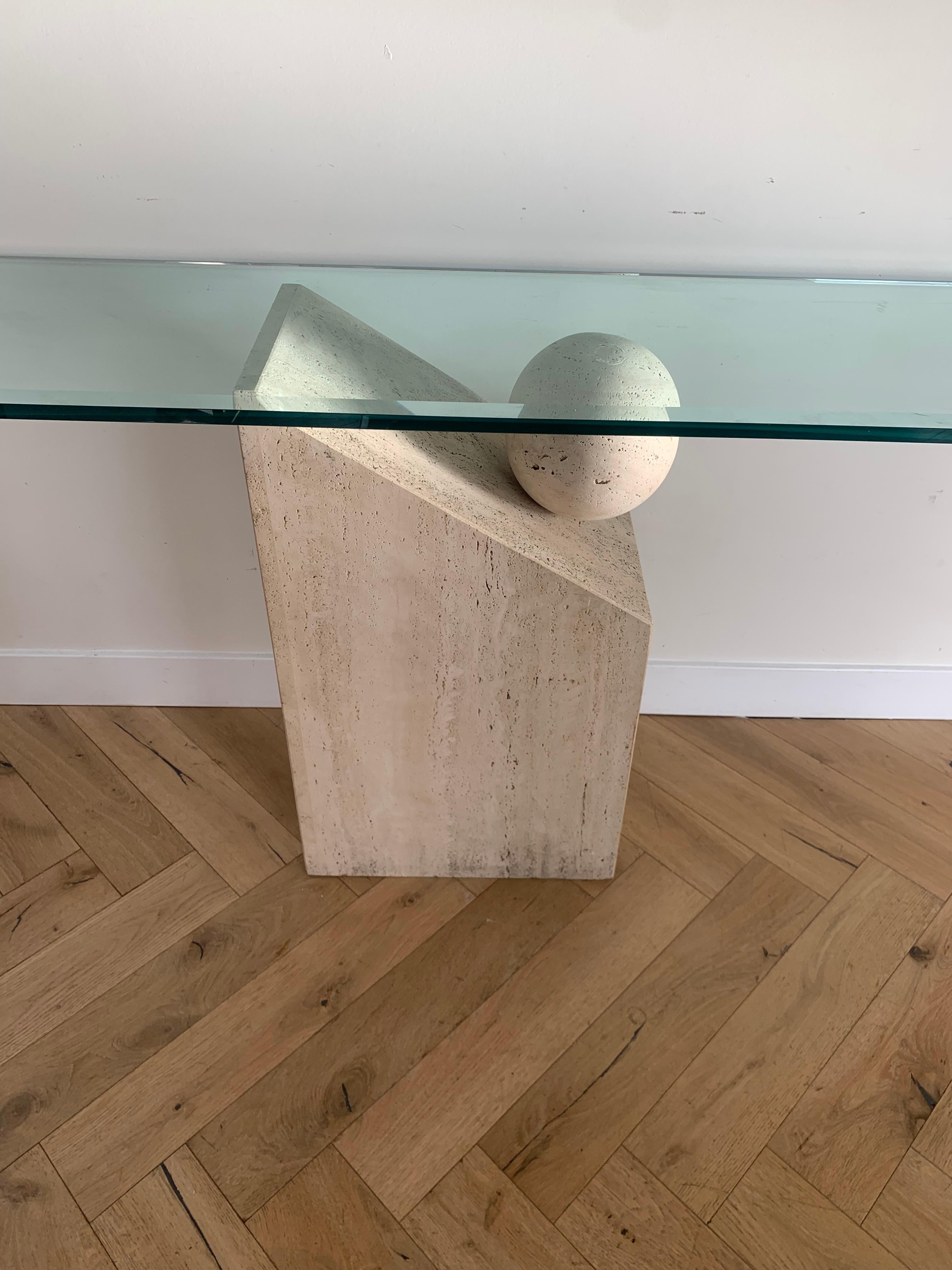 A spectacular vintage Italian postmodern console table hand-carved out of raw travertine and featuring an orb suspended on a tilted plinth, upholding a thick (.75” thick) beveled glass top. From Italy, circa mid 1970s. An asymmetrical tour de force