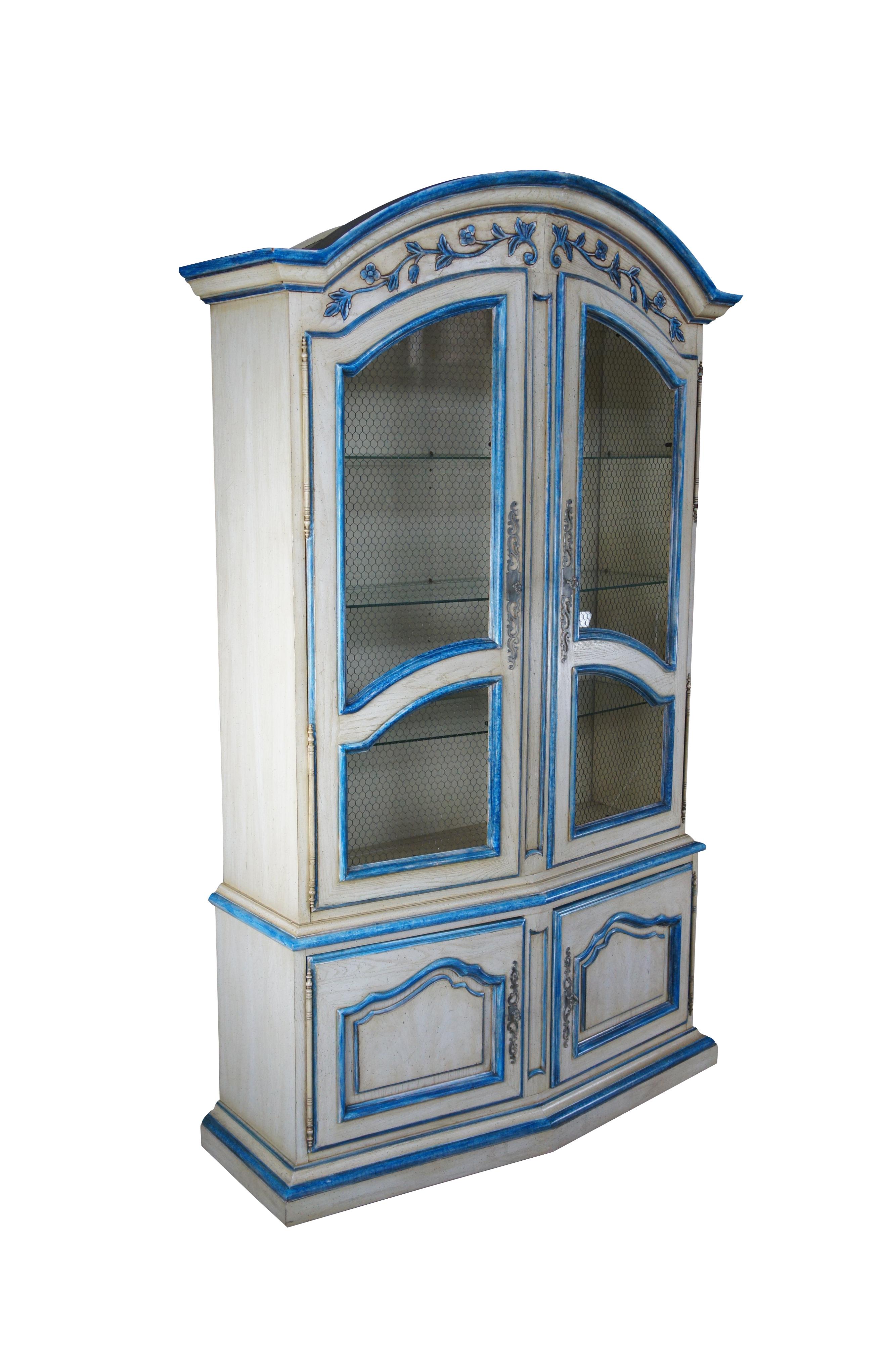 A beautiful farmhouse curio cabinet or showcase, circa 1940s.  Drawing inspiration from French Country and Italian Provincial design.  Made from oak with an off white finish trimmed in blue.  Features a domed hutch with foliate carved crown, chicken