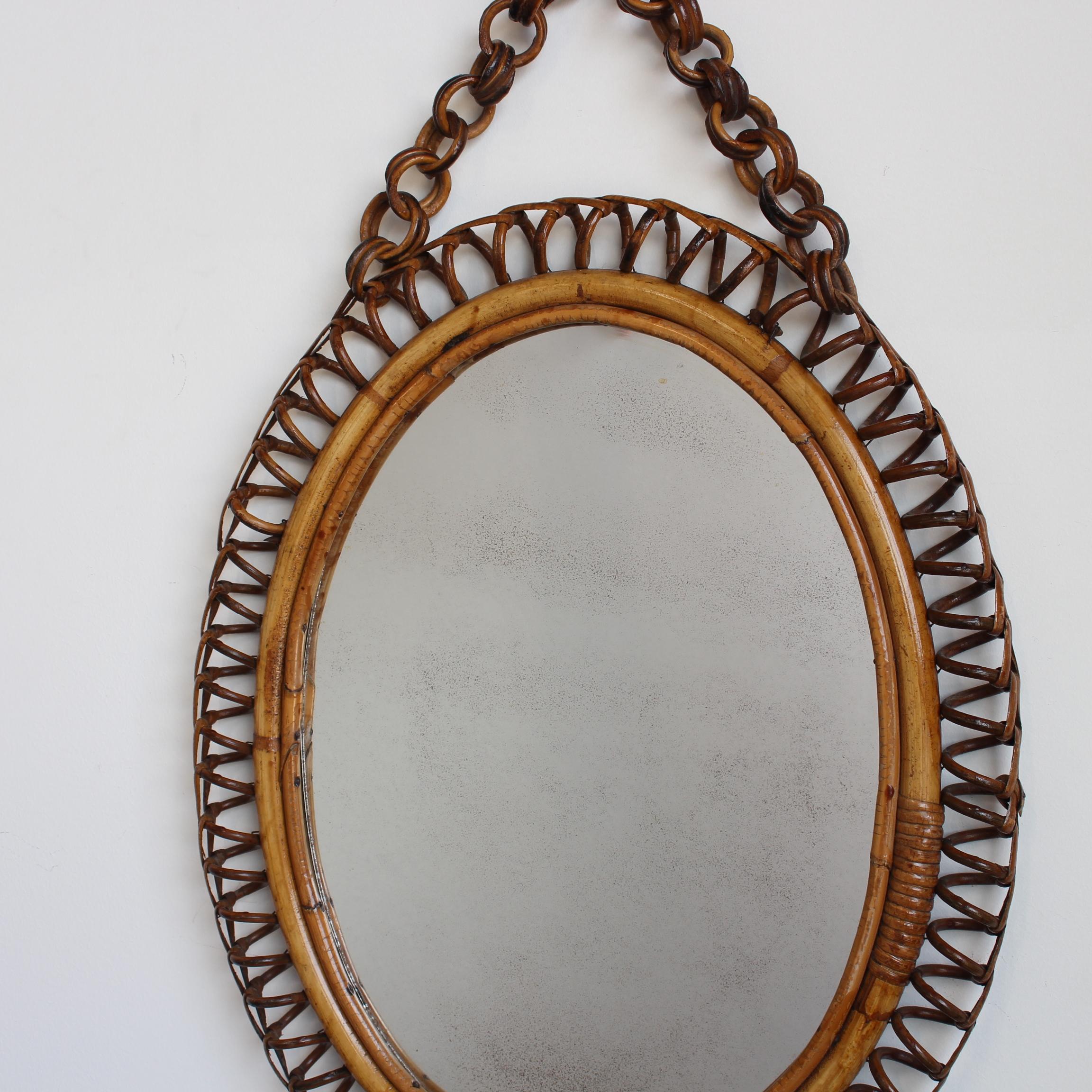 Italienischer ovaler Wandspiegel aus Rattan (ca. 1960er Jahre). Dieser Spiegel hat eine sehr charmante Form mit Rattanspiralen, die den Spiegel einrahmen. Die funktionale Rattankette zum Aufhängen sorgt für zusätzlichen Reiz. Der Spiegelrahmen weist