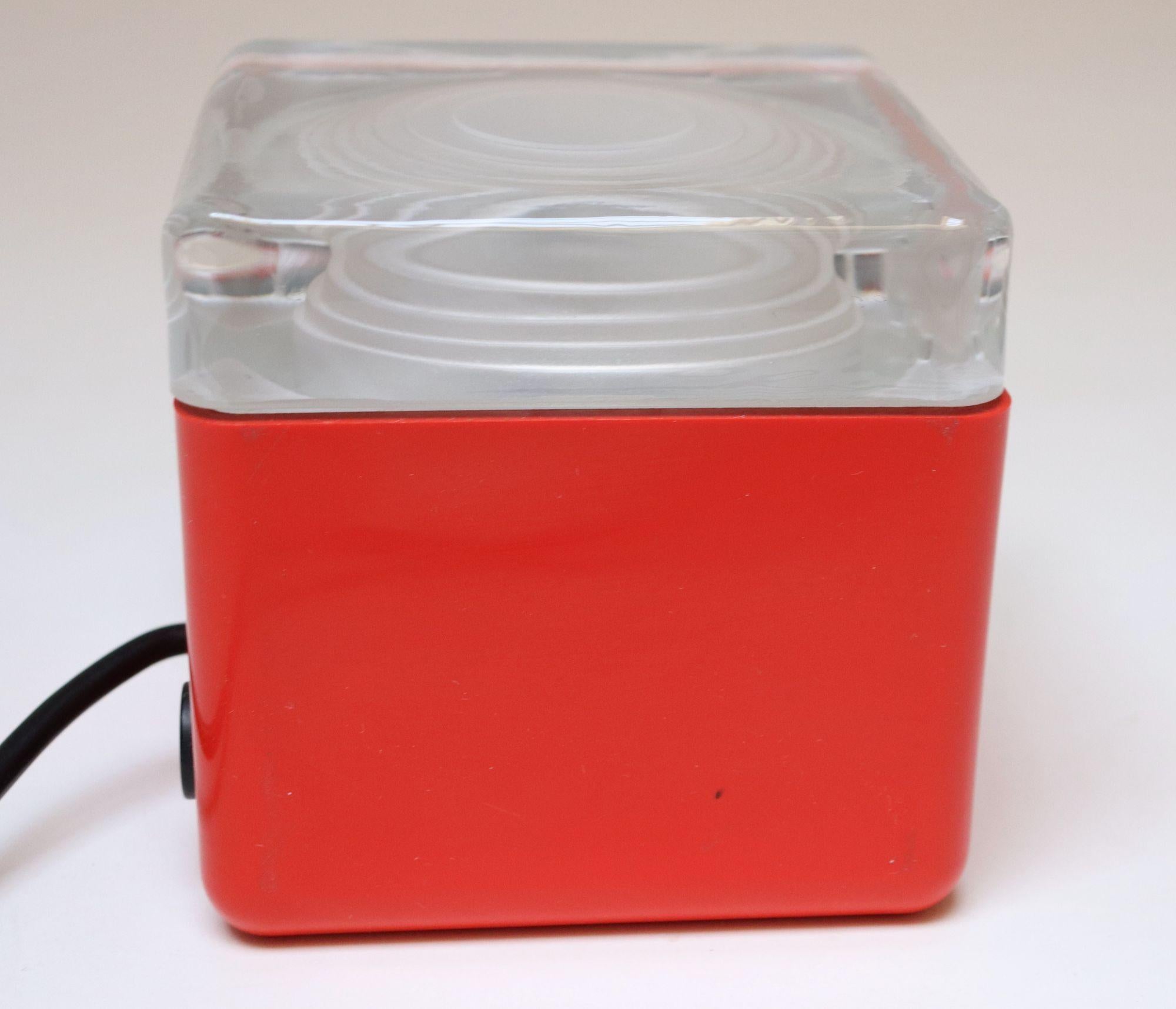 Petite cube lamp in red plastic with dense glass top diffusing a warm, pleasant light attributed to Lamperti Robbiate (ca. 1970s, Italy).
Black push button on/off found on the back of the lamp.
Excellent, vintage condition with only minimal wear