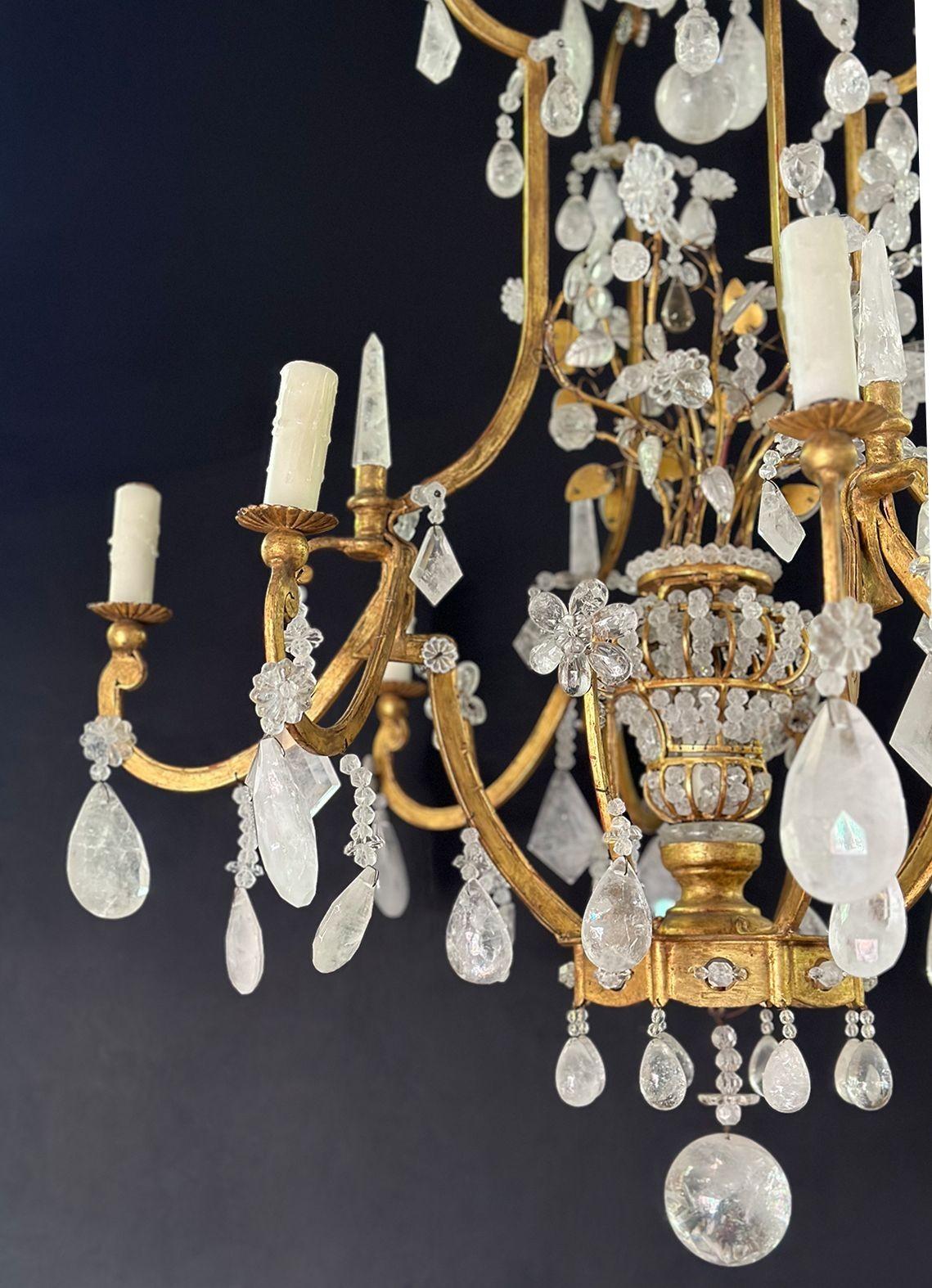A vintage Italian chandelier fixture made in the 20th Century, consisting of a gilt metal frame and rock crystal shapes; mostly drop and spheres. It also consists of crystal garlands around the piece. It is decorated in the center with floral