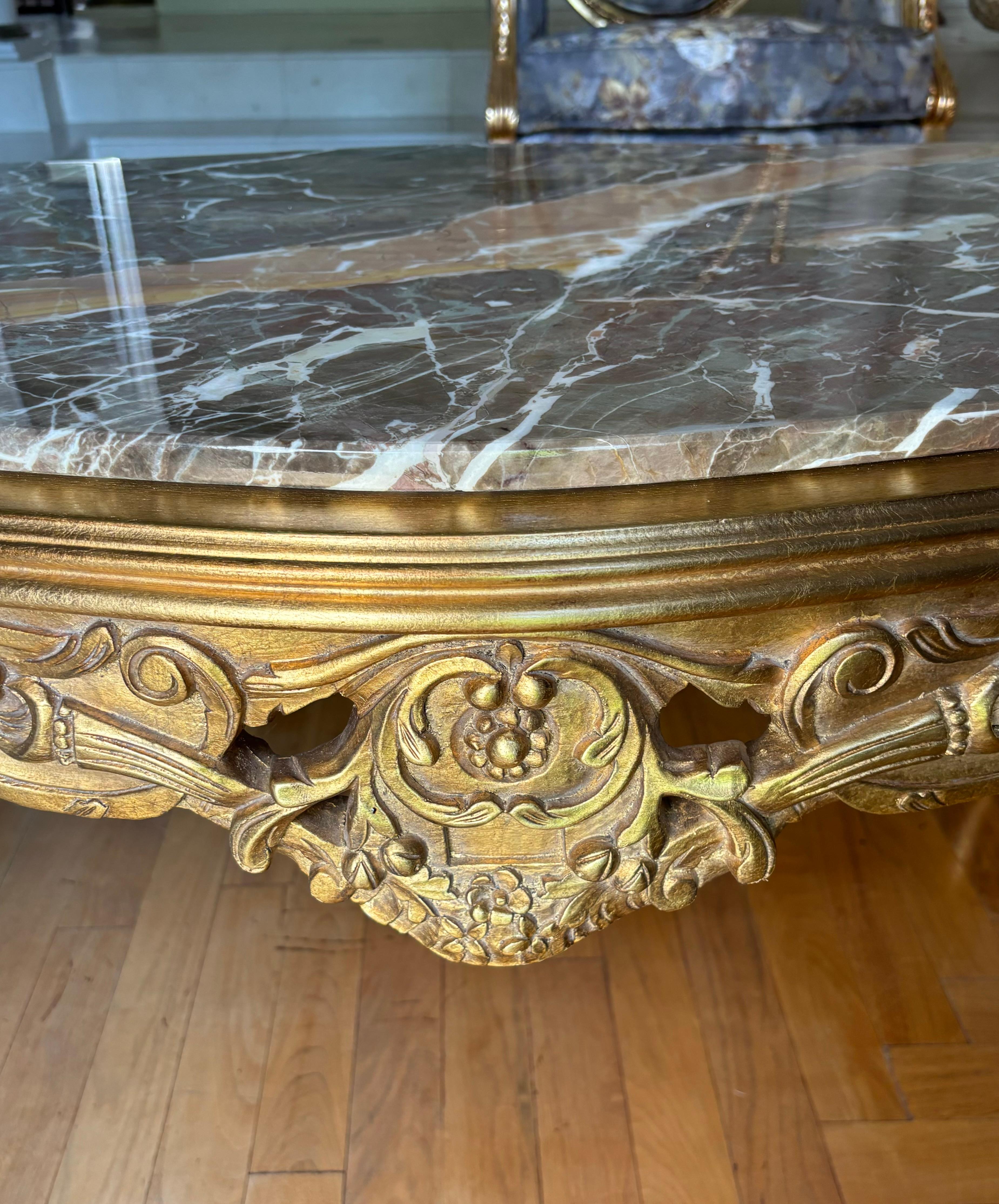 Table basse en bois doré sculpté de style rococo italien avec un magnifique plateau en marbre Macchiavecchia biseauté réalisée par Asnaghi Interiors en Italie. Le plateau en marbre brun repose sur une base en bois doré finement sculptée avec des