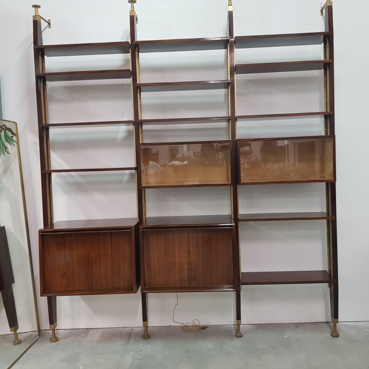 Italian 1960s rosewood bookcase composed by four uprights, shelves and storage cabinets. Brass hardware. Shelves are adjustable in their height. This book case takes inspiration from Albini bookcase since it is based on the floor and fixed to the