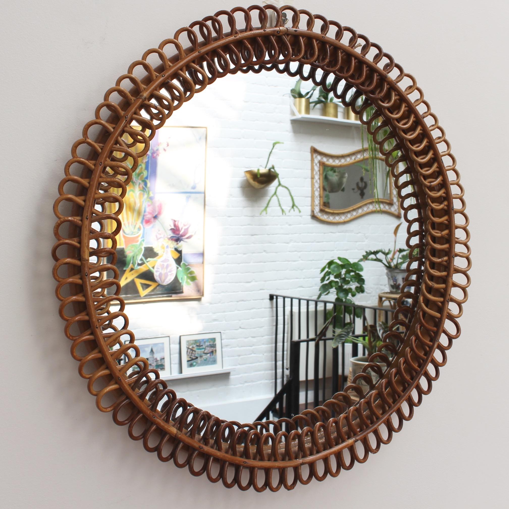 Italian rattan round wall mirror (circa 1960s). This mirror has a very delightful circular sun shape framed with rattan figure-eight resembling pretzels. There is a characterful, aged patina on the mirror frame and overall, the piece is in good