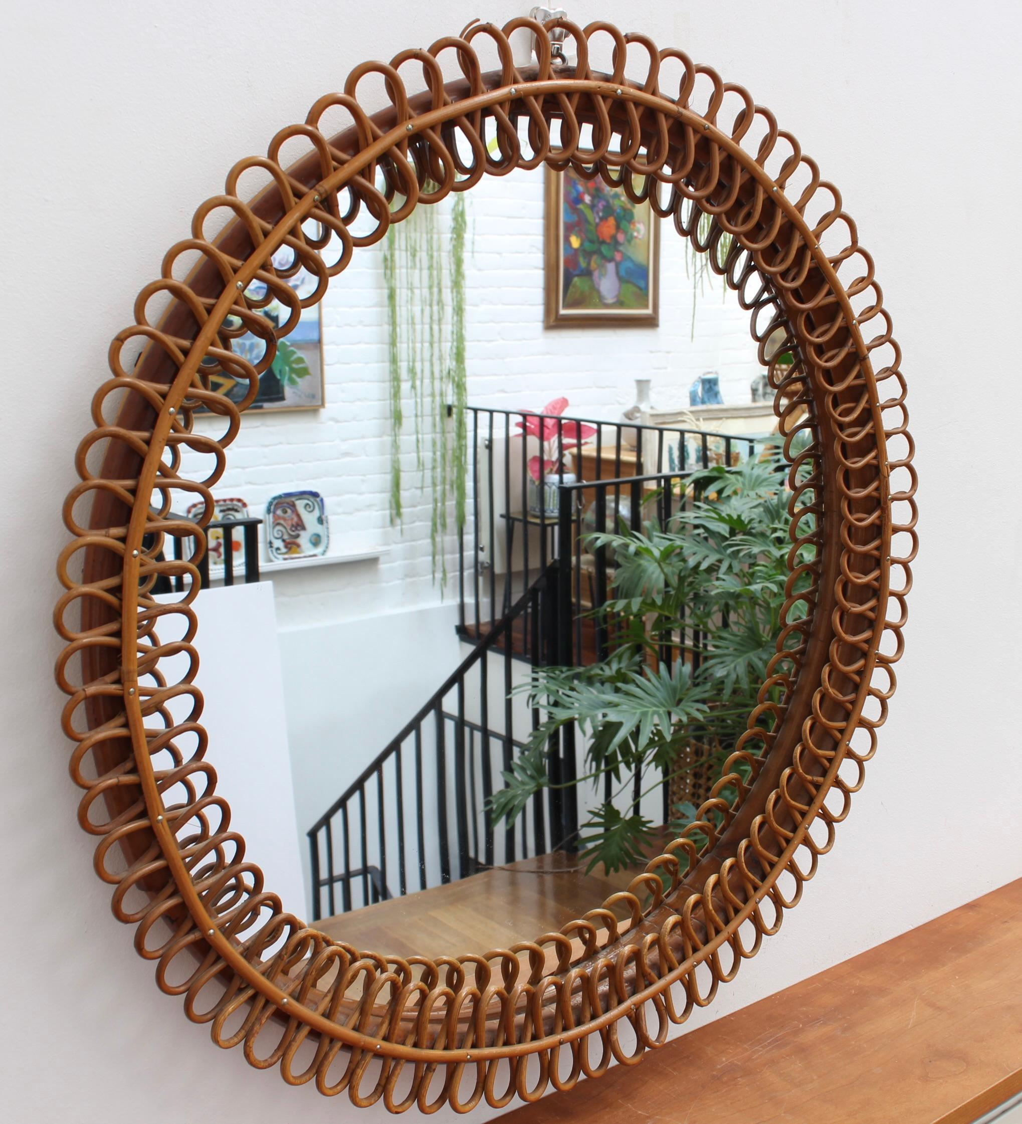 Mid-Century Italian rattan wall mirror (circa 1960s). This mirror has a very delightful  circular sun-shaped frame with rattan figure-eights resembling pretzels. There is a characterful, aged patina on the mirror frame and overall, the piece is in