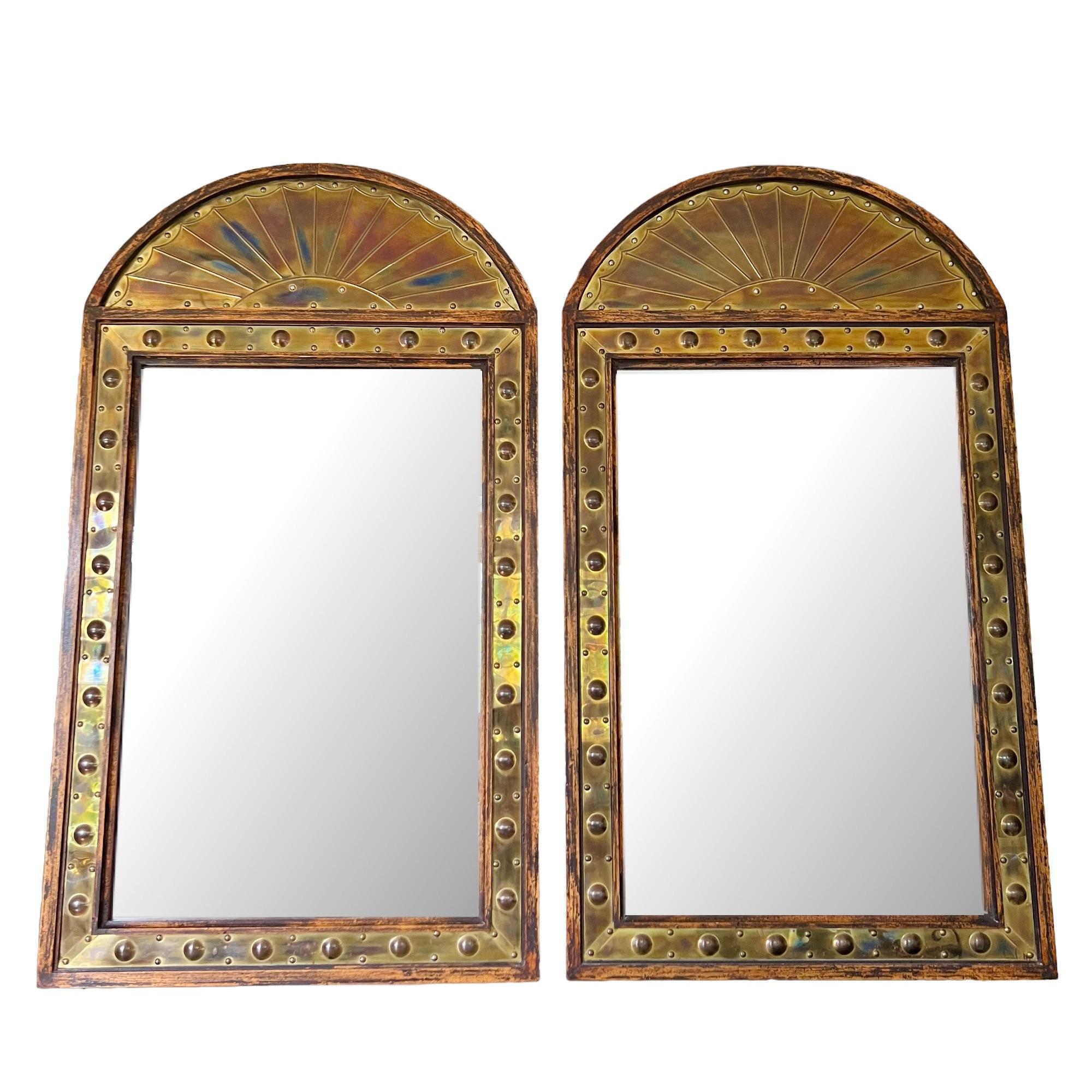 A vintage pair of Italian brass clad and wood framed arched wall mirrors by Sarreid Ltd circa 1970's. Spanish style design featuring studded brass repoussé panels and fan detail dome top set in patinated wood framing.

Dimensions: 24