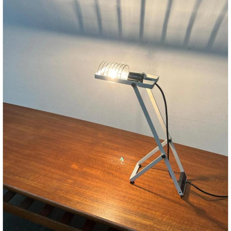 Rara lámpara de mesa de la serie Sintesi, del fabricante italiano Artemide y obra de Ernesto Gismondi.

La lámpara muestra los elementos característicos de la serie Sintesi, los puntales negros y el marco blanco con junta. La lámpara está formada
