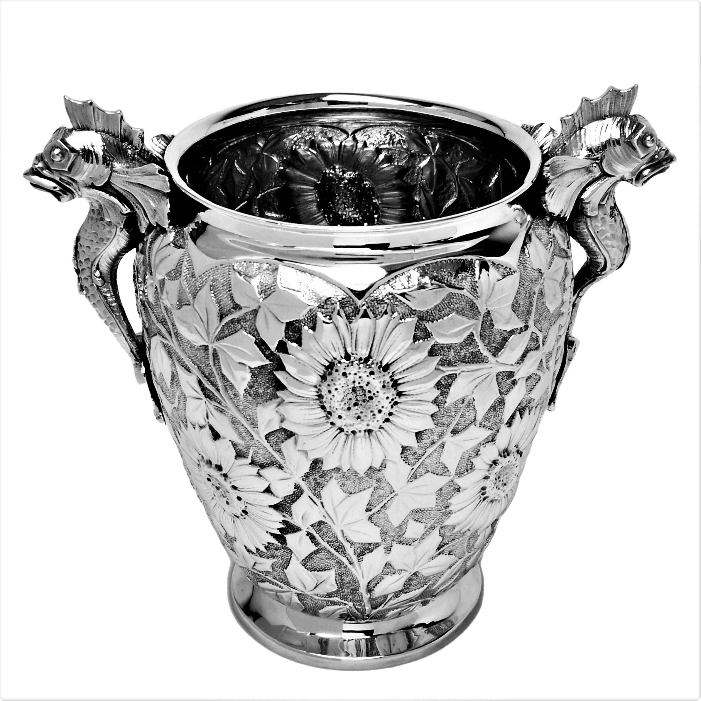 A beautiful vintage solid silver wine cooler with an unusual floral chased design covering the body of the Cooler. The Champagne Ice Bucket has a pair of medieval style fish / dolphins shaped to form handles. This Champagne Cooler is also suitable