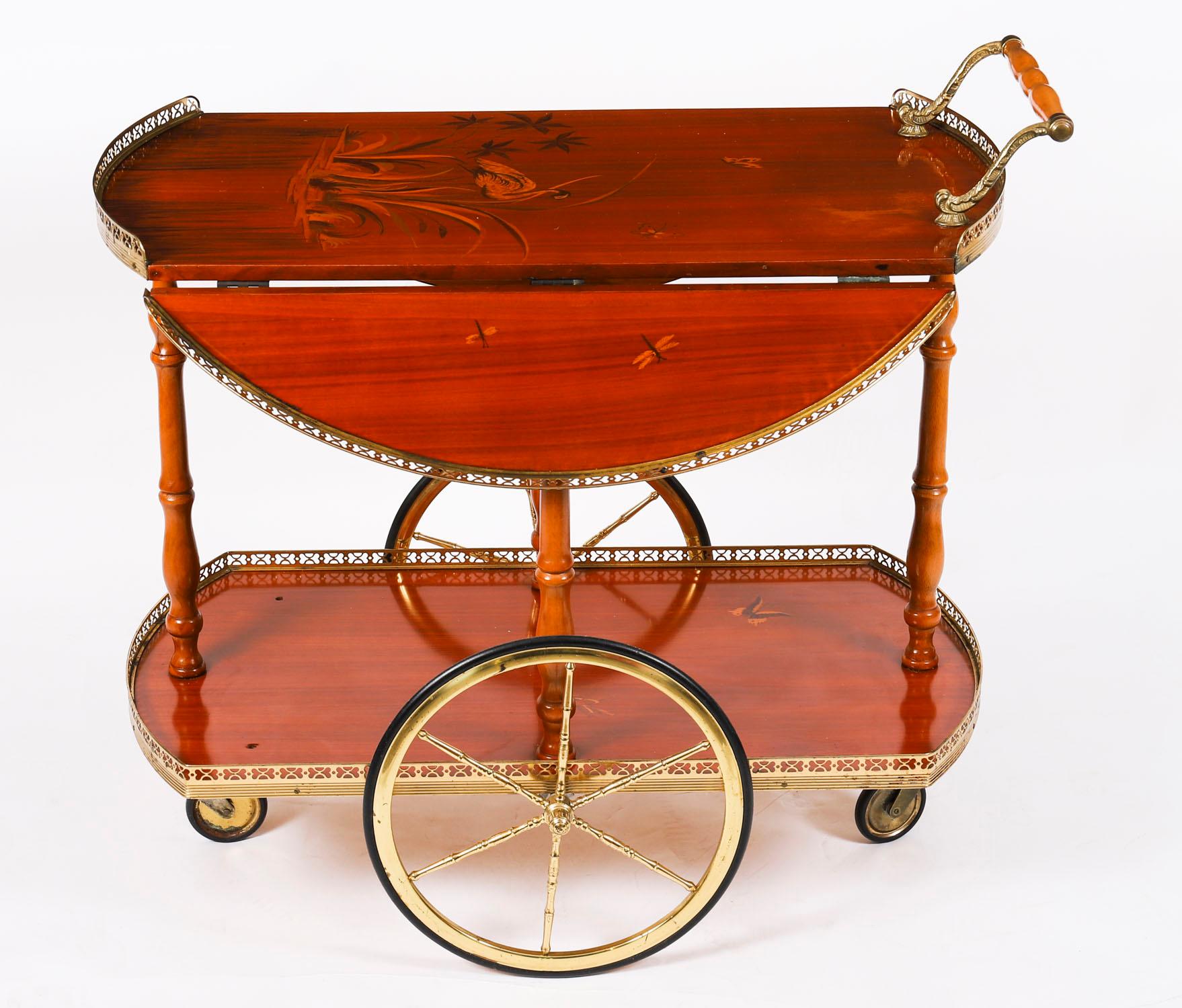 Si tratta di un divertentissimo carrello portabevande italiano a due piani di Sorrento, risalente alla metà del secolo scorso,

Il piano ovale con alette con decorazioni a intarsio di una gru, fiori, farfalle e bordi in ormolu a gallerie, il piano