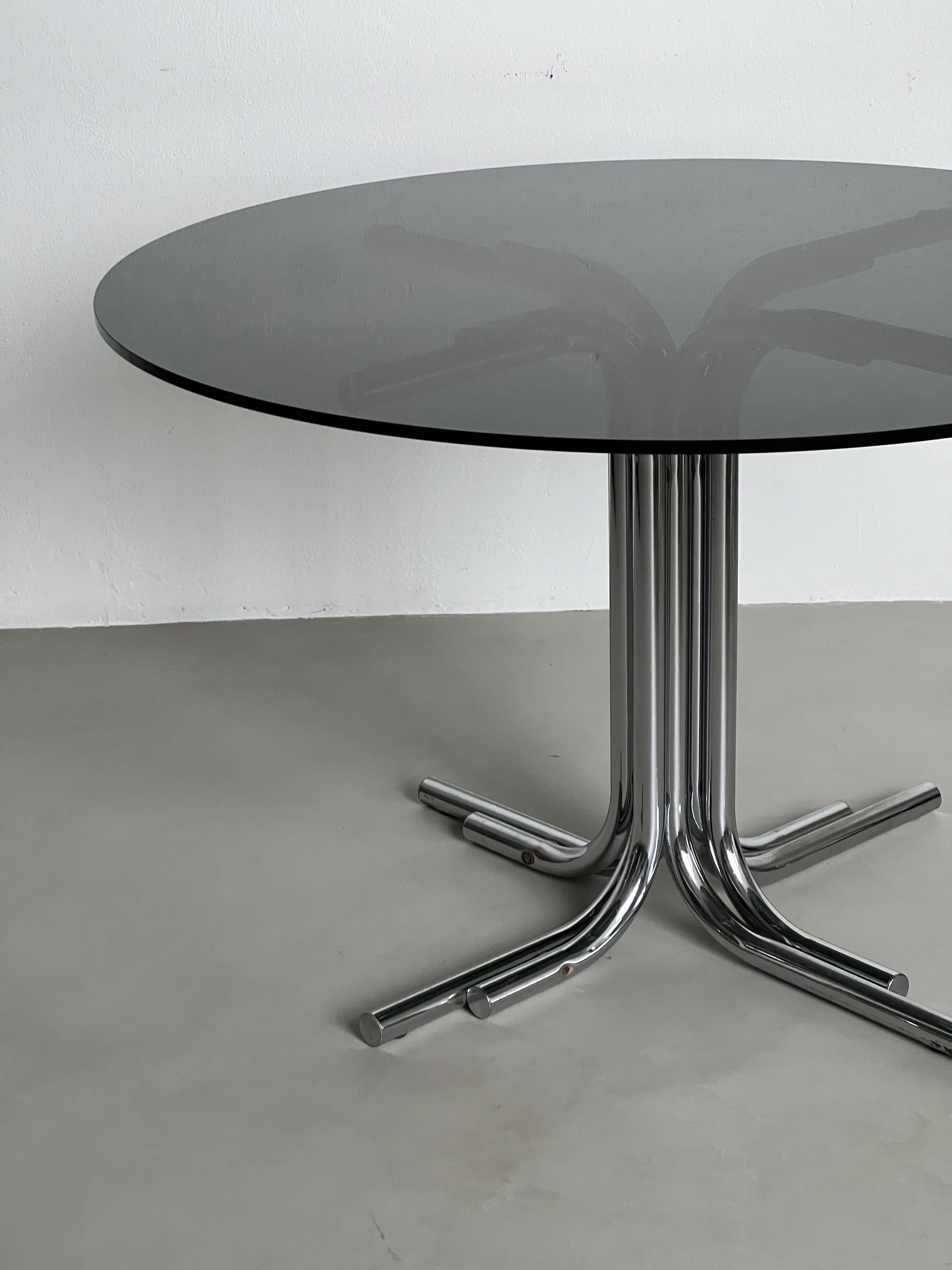 Offered for sale is a stunning and timeless Space Age dining table, with tubular legs in chromed metal and a round smoked glass top with squared edge. Designed and manufactured most likely during the Seventies, it's anonymous, but the choice of