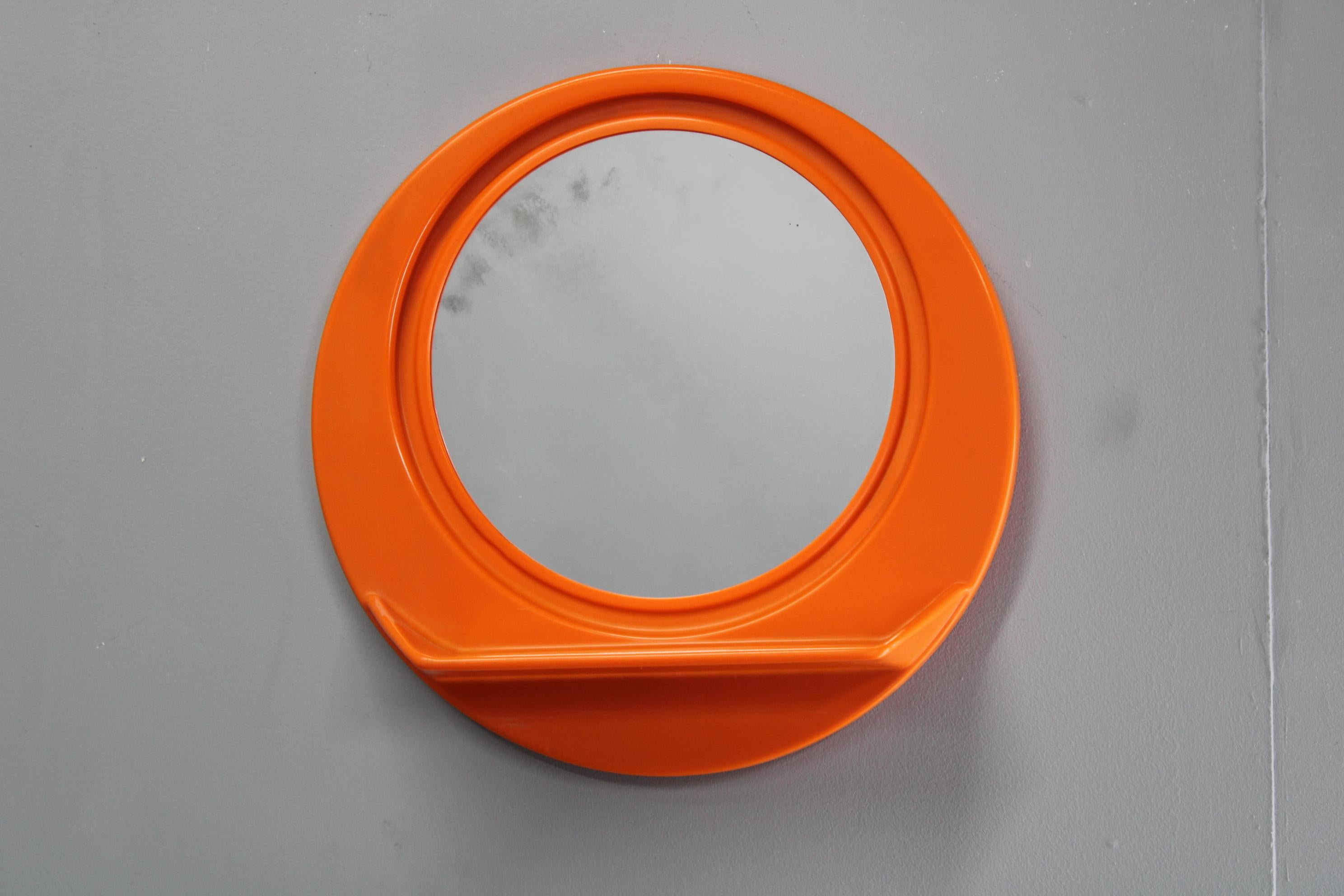 Miroir mural rond italien des années 1970, fabriqué en plastique orange vibrant, avec une étagère intégrée pour plus d'utilité et un style rétro audacieux. Cette pièce emblématique de l'ère du design de l'Icone allie un rangement fonctionnel à des