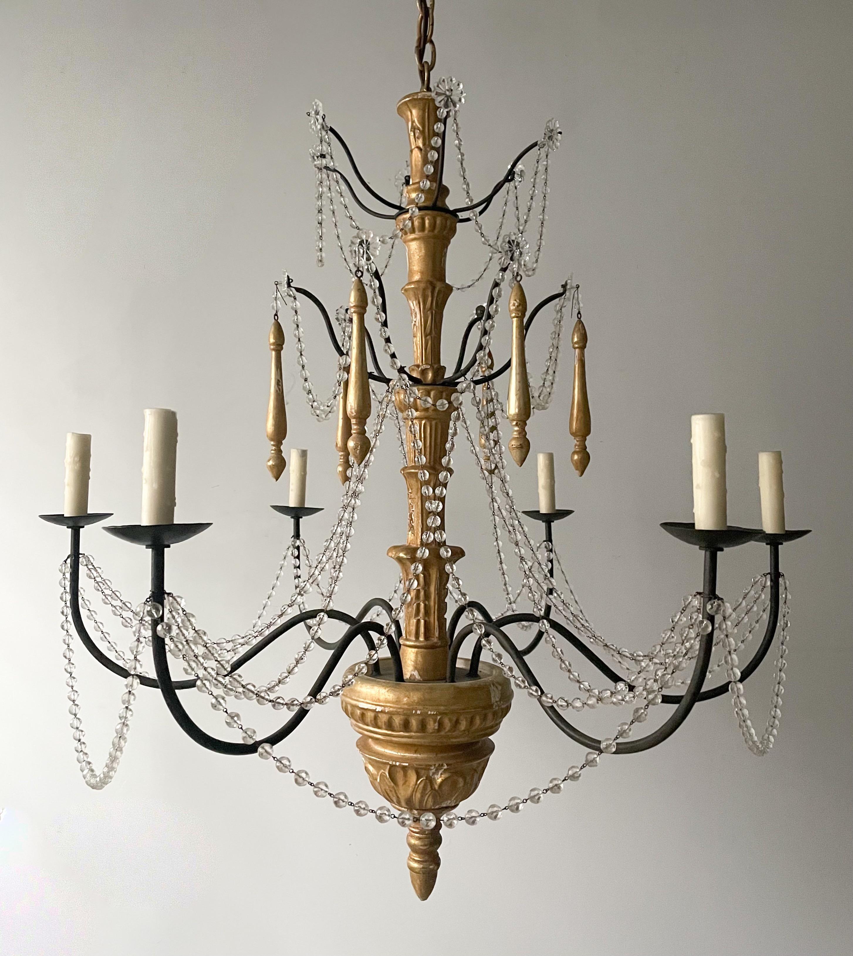 Gorgeous, vintage giltwood, iron and crystal chandelier in the Genovese style.

The chandelier consists of a carved wood column in a distressed, gilded finish and decorated with crystal bead garlands. 

The chandelier is wired and in working