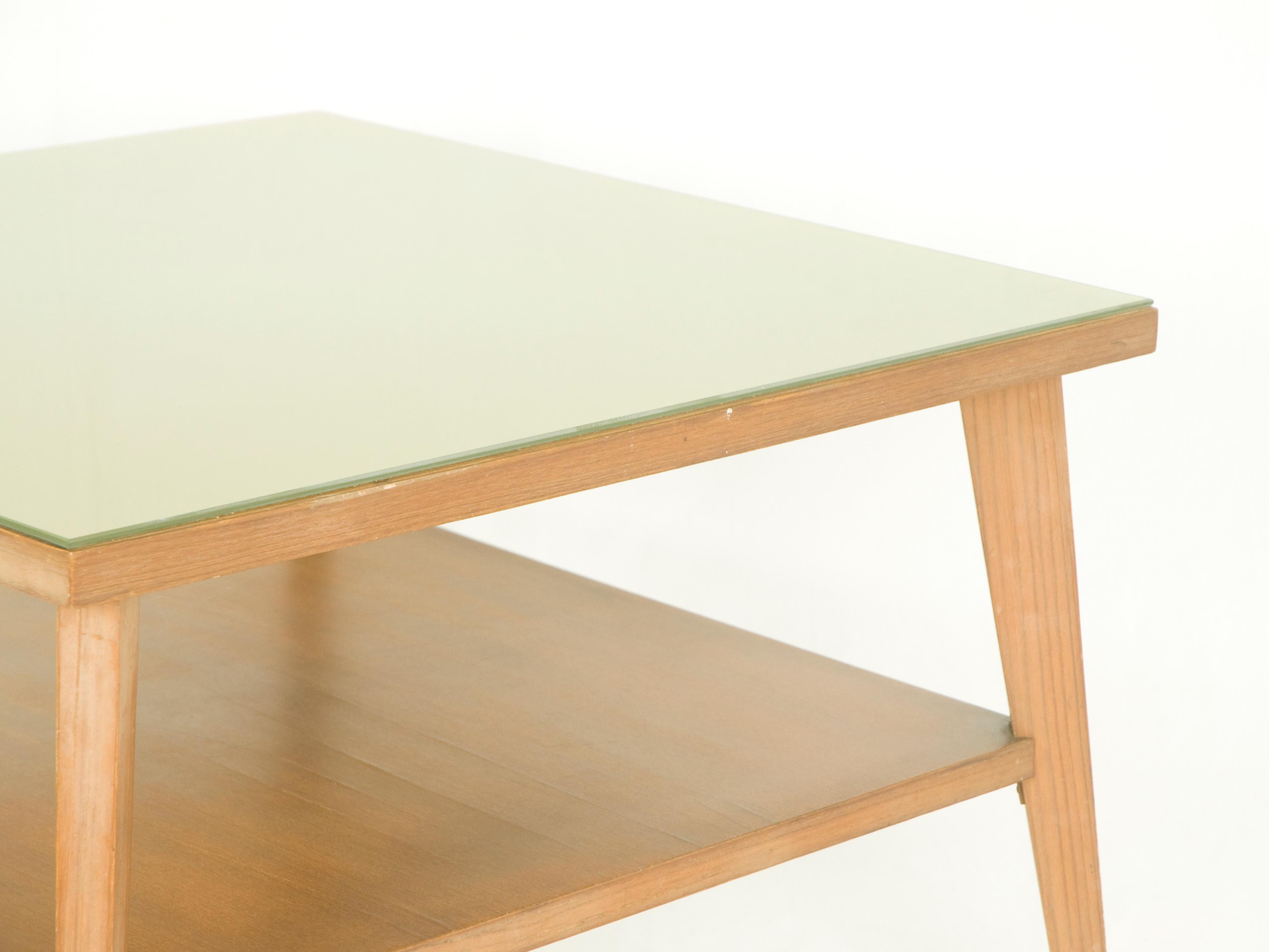 Dieser quadratische Couchtisch besteht aus einer Teakholzstruktur mit einer grünen Glasplatte. Es verfügt über zwei nützliche Regale. Das Glas der Oberseite ist klar, aber mit einer hellgrünen Metallschicht auf der Rückseite überzogen. Die