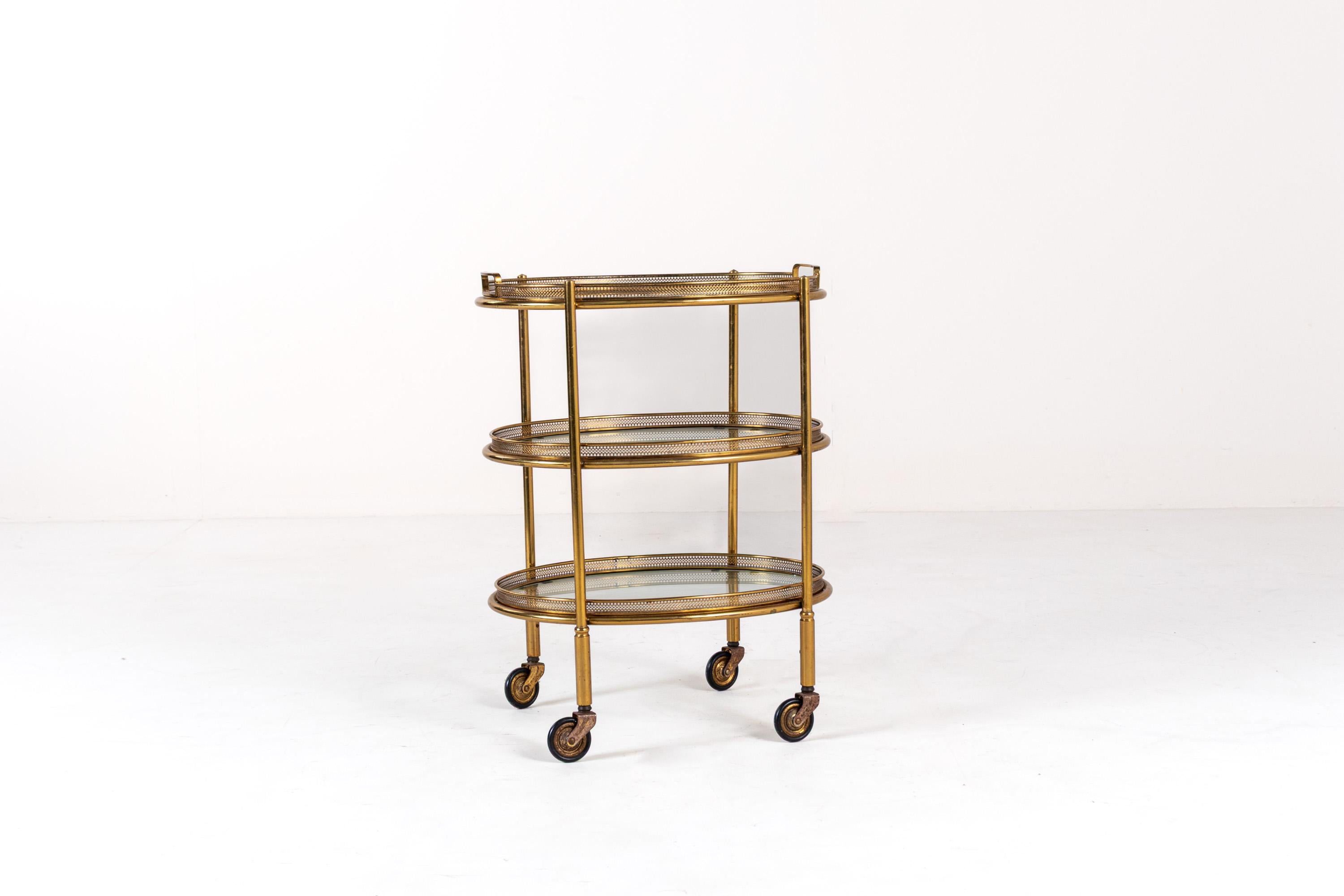 Chariot de service ovale en laiton et verre avec trois plateaux amovibles. L'étagère a un design compact, veillez donc à vérifier les mesures pour vous assurer qu'elle s'adapte à votre espace.