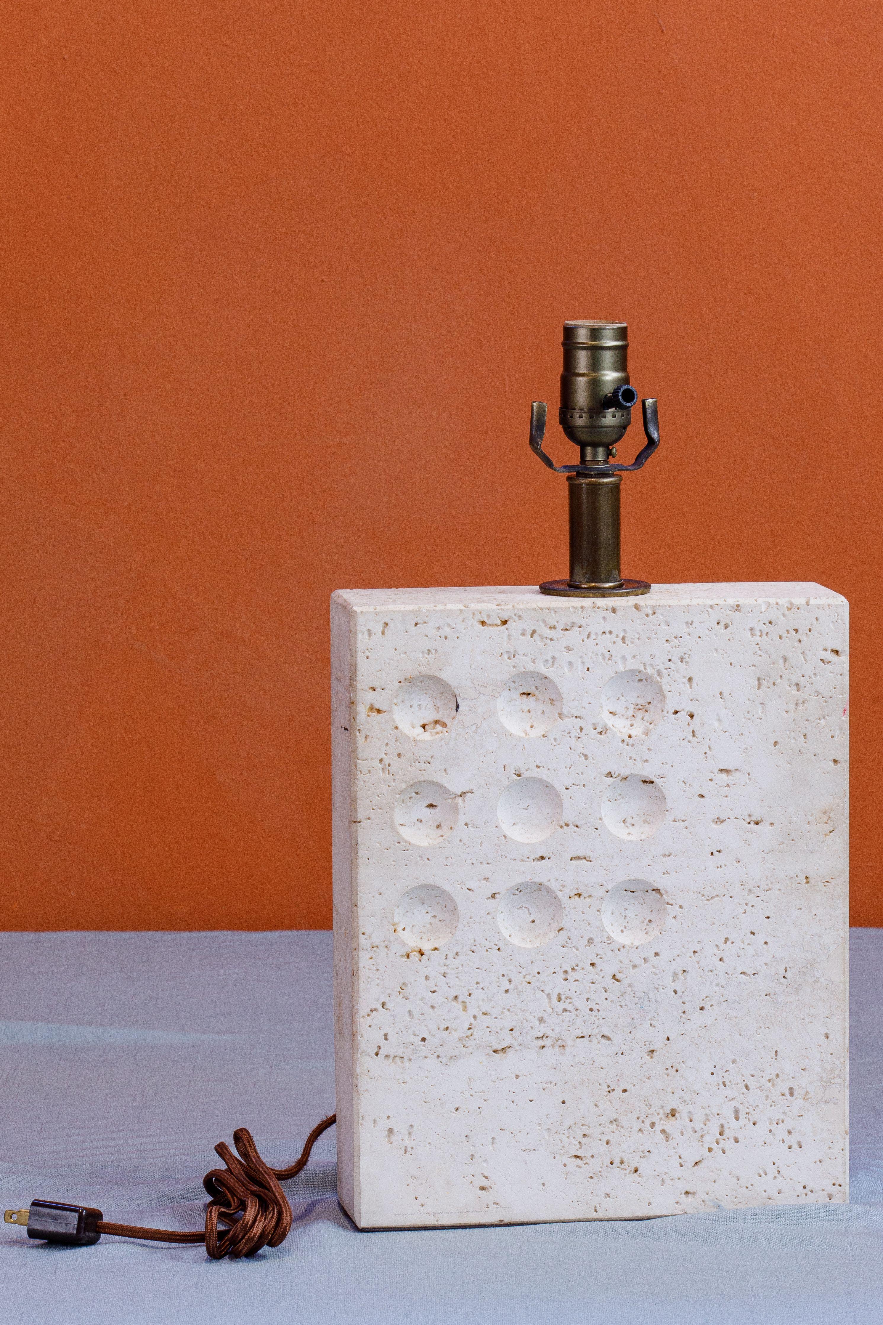 Stunning Italian travertine table lamp in the style of Goffredo Reggiani circa 1960s. Solid travertine lamp with a grid of 9 carved / impressed circular designs. Brass stem, harp and finial. Takes one standard base light bulb. The lamp has been