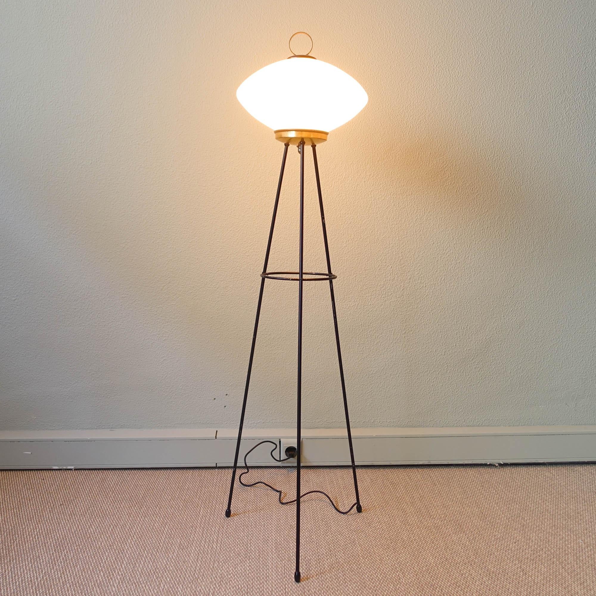 This Italian design tripod floor lamp was designed and produced in Italy during the 1950s, with a design reminiscent of Stilnovo. The lamp stands on tripod legs and is made out of a brass and black lacquered metal structure. Finished on top with an