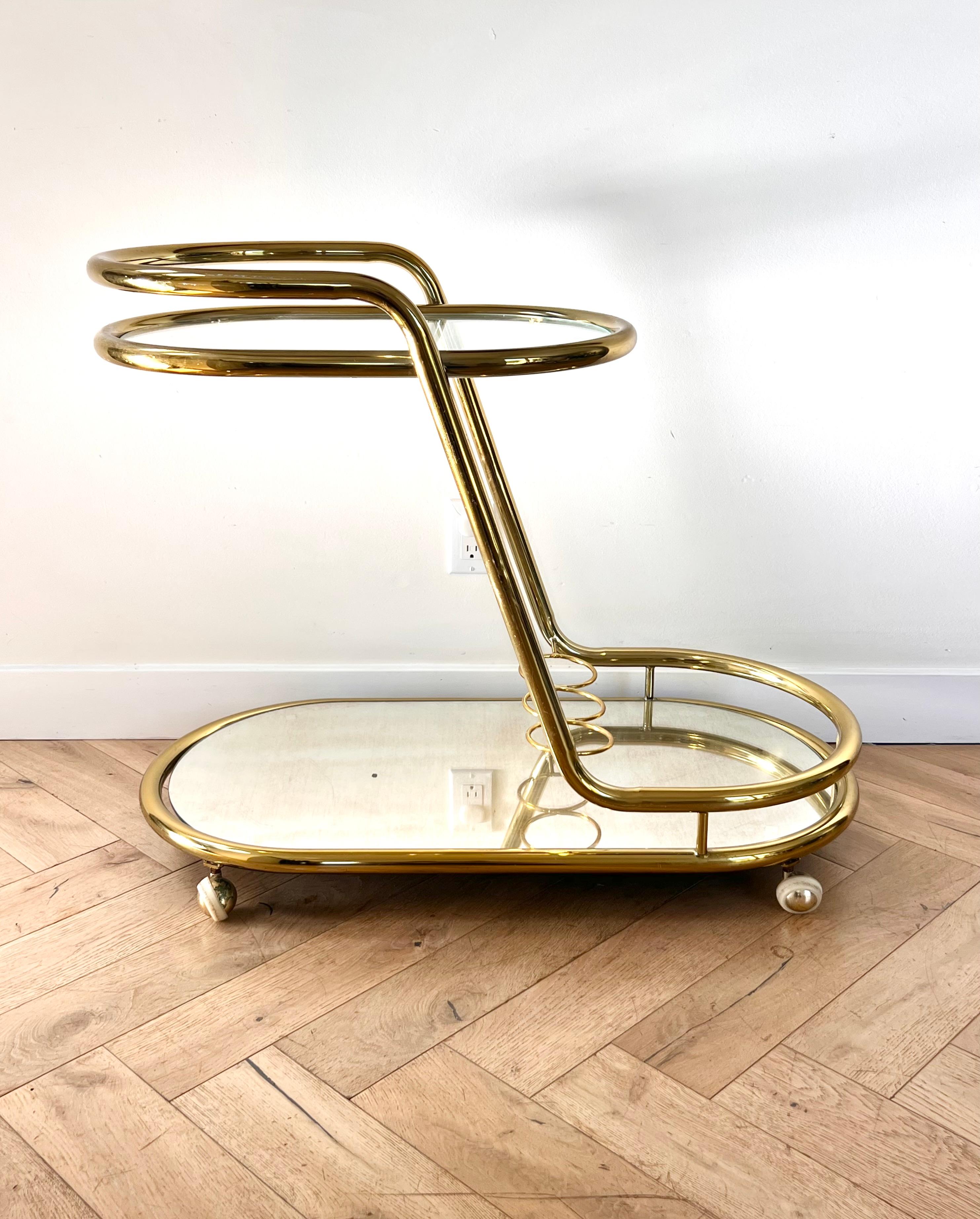 ITALICS: a midcentury two-tier tubular Italian bar cart attributed to Morex, circa 1970s. Featuring a slanted frame in gold plated chrome with glass top and a mirror base, as well as bottle enclaves on the second tier. Both shelves are removable for