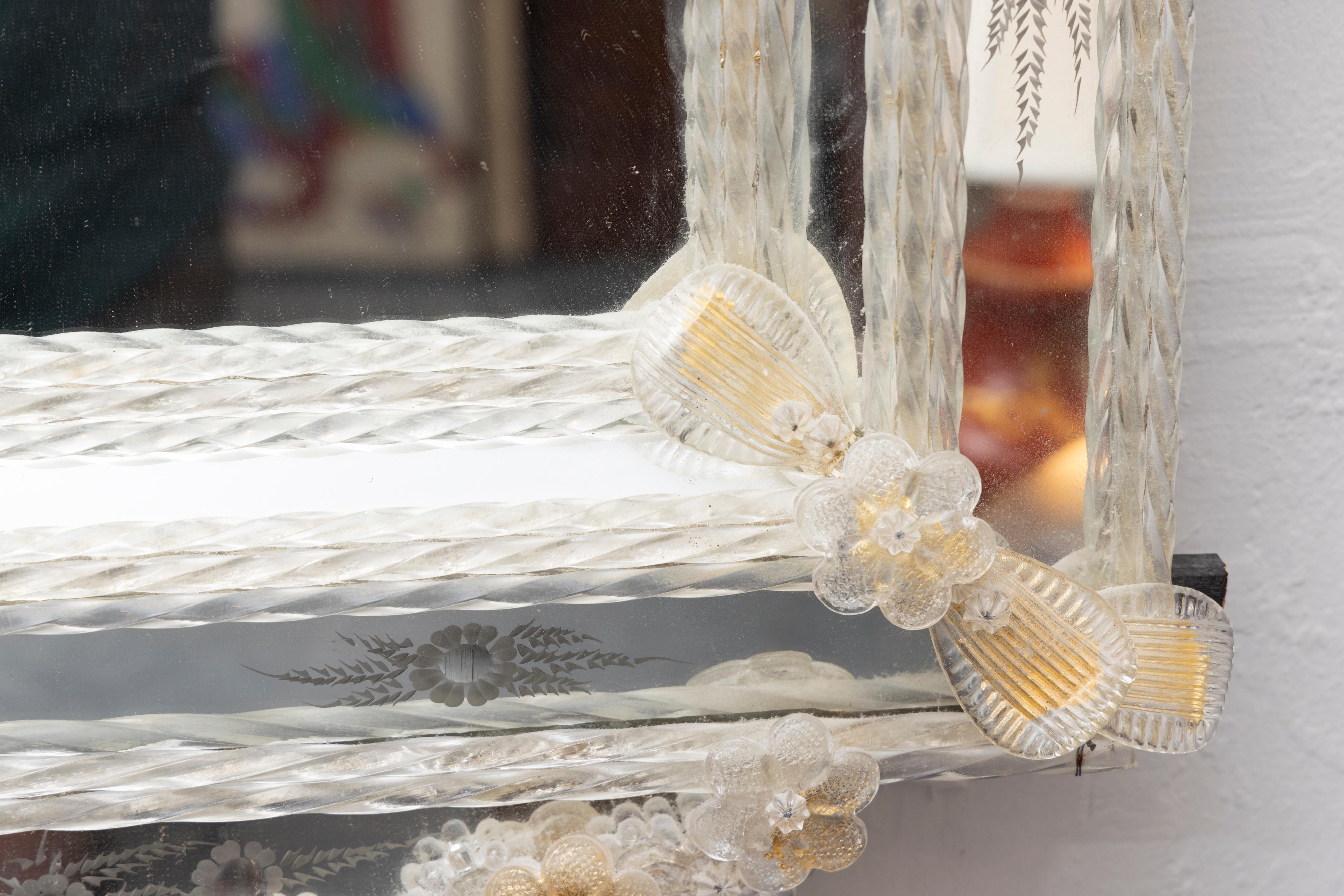 Il s'agit d'un joli miroir vénitien italien classique et romantique dont la plaque centrale est entourée d'un cadre composé de panneaux de verre gravé encadrés par des tiges de verre clair torsadées, accentuées par des fleurons de verre clair